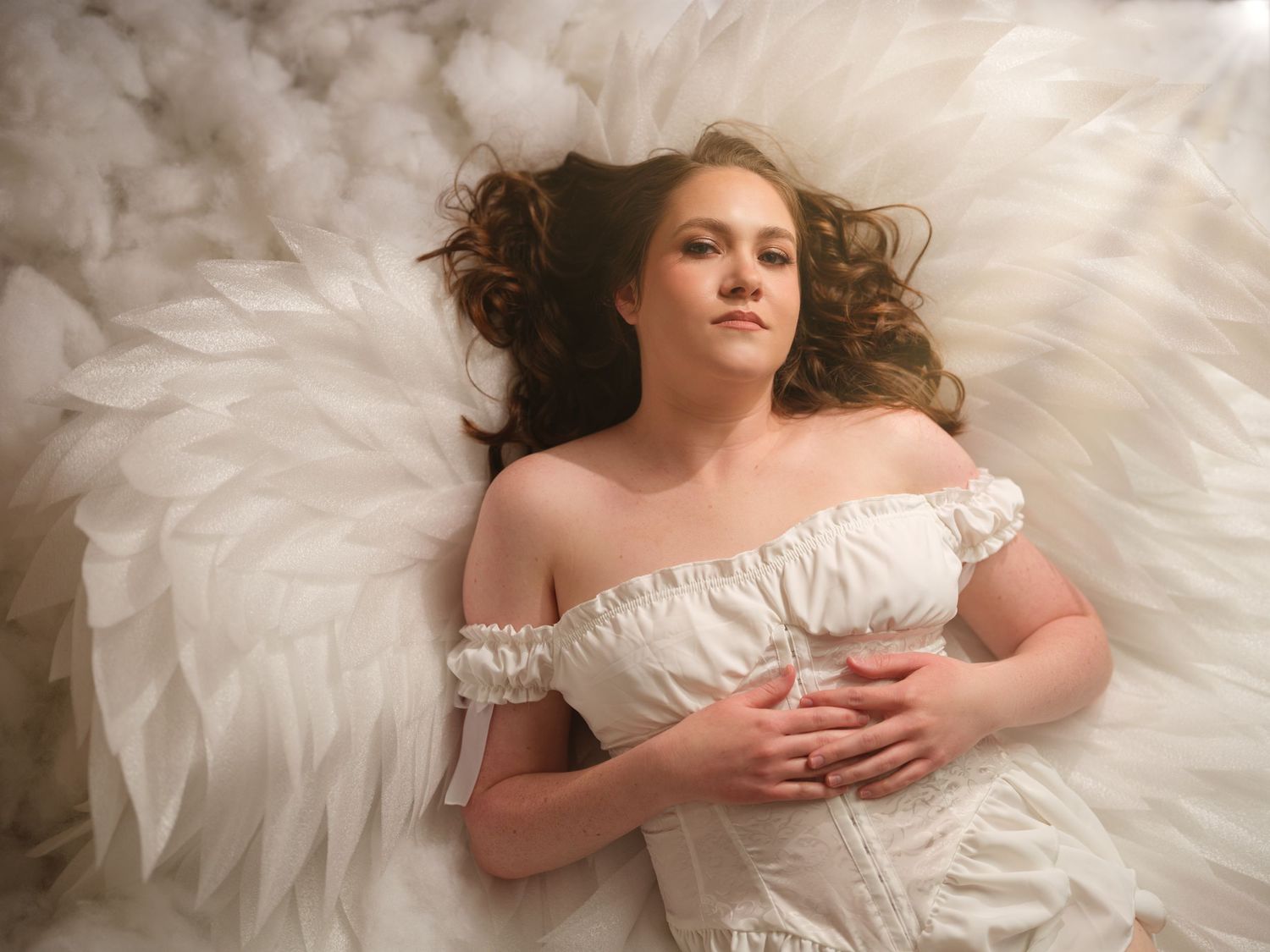 A dreamy bridal portrait shows a figure reclining on white tulle fabric with soft lighting and romantic styling.