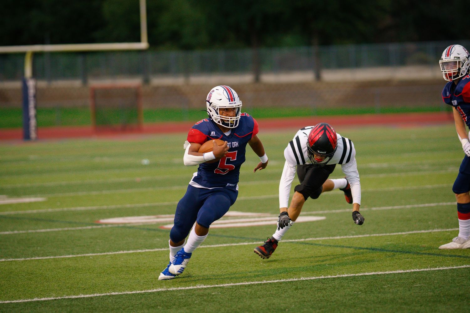 Football players in white and blue uniforms crouch in formation on a grass field during a game.