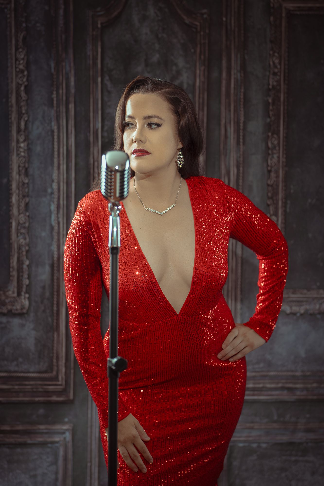 Dramatic portraits in sparkling red sequin dress with vintage microphone against dark background.
