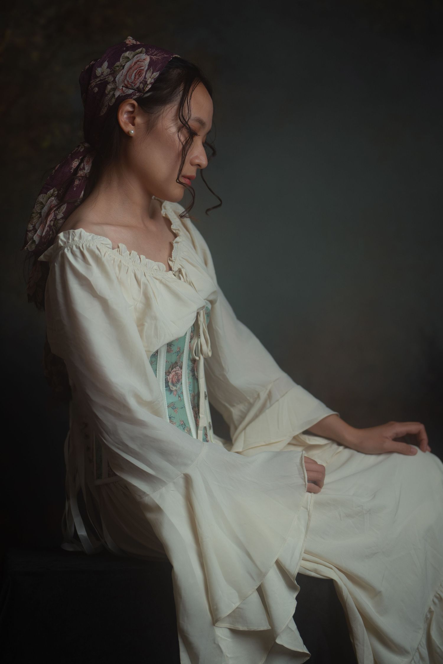An ethereal portrait series featuring a model in a flowing white dress with ruffled sleeves in a dark moody setting.