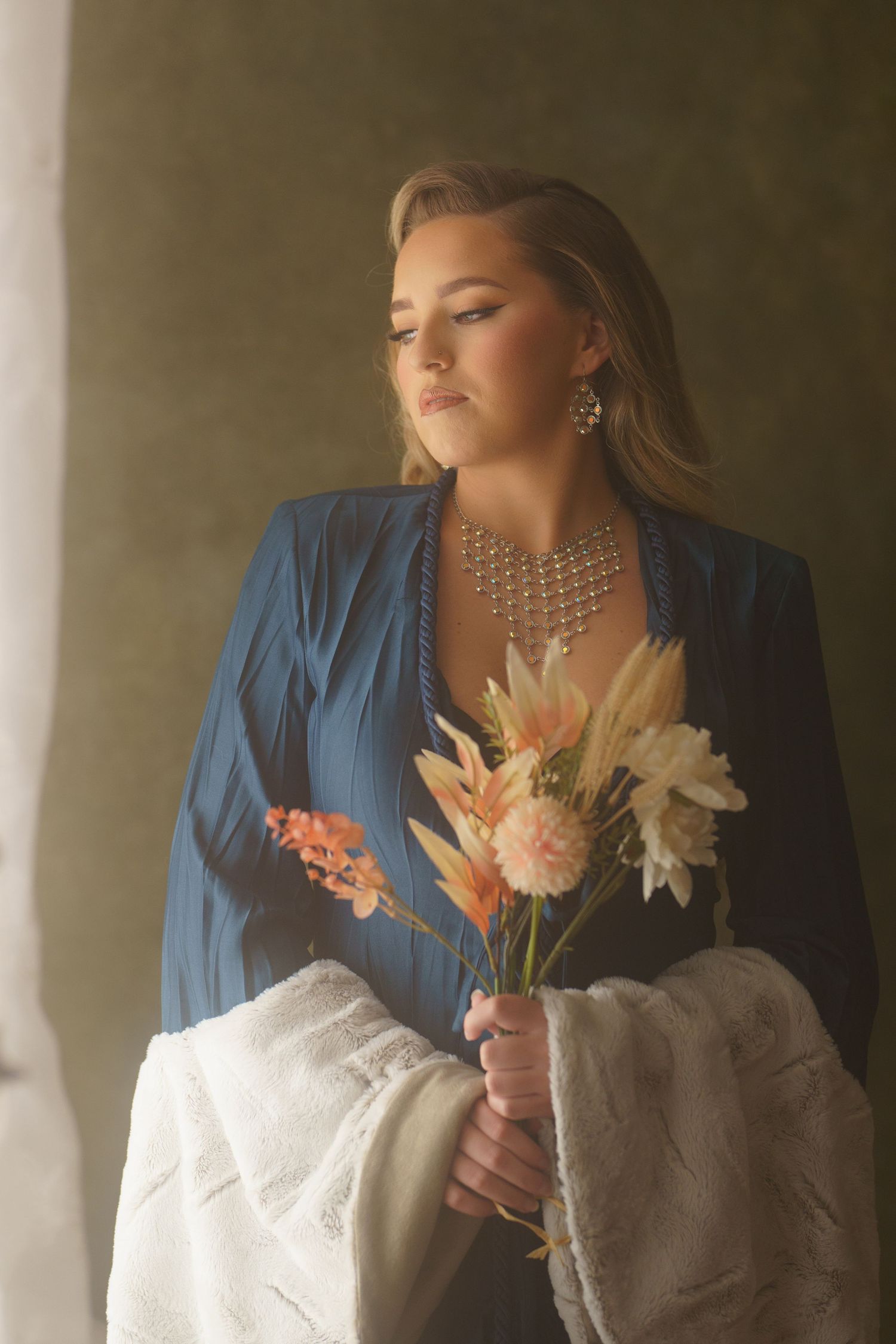Elegant fashion portrait with white flowers and blue jacket against light backdrop.