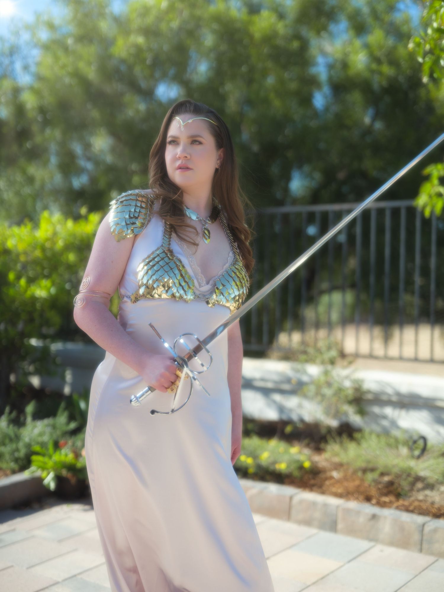 Person in flowing pink dress with metallic accents standing in sunny garden setting.