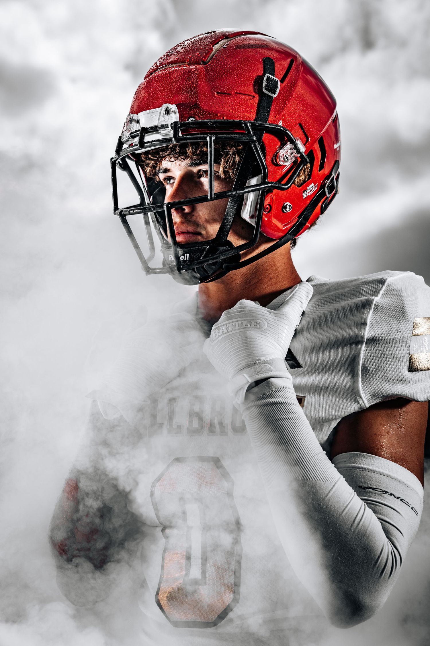 Football player wearing red helmet and white jersey emerges from dramatic smoke effect in sports photo series.
