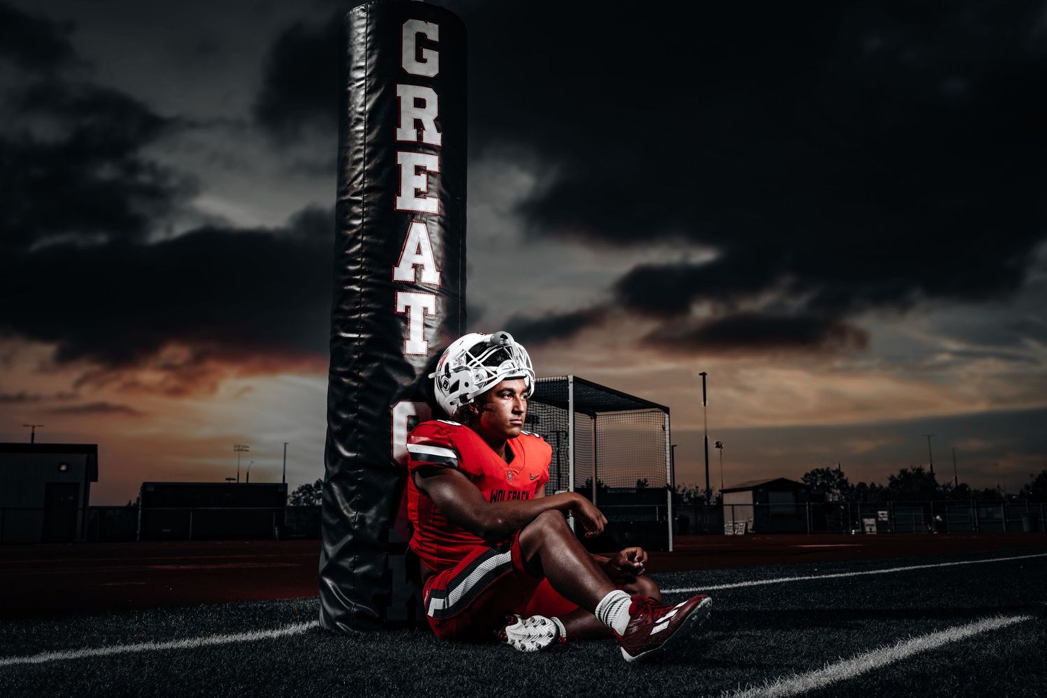 A football player in red uniform runs with the ball at sunset on a dark field during practice.