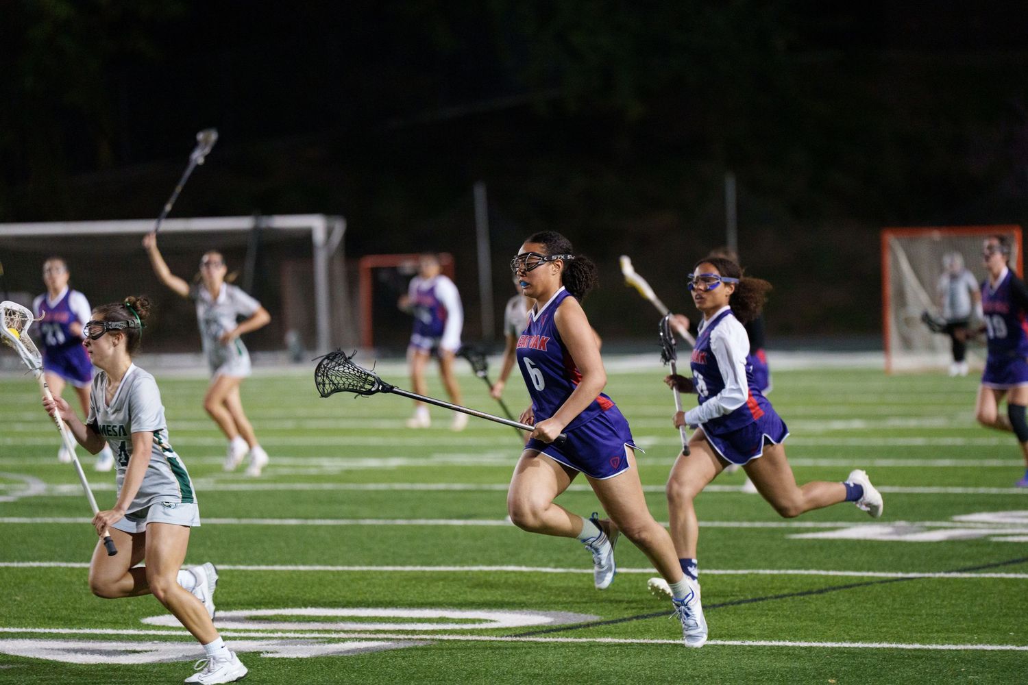 Field hockey players perform stretching exercises on a turf field during a team practice session.