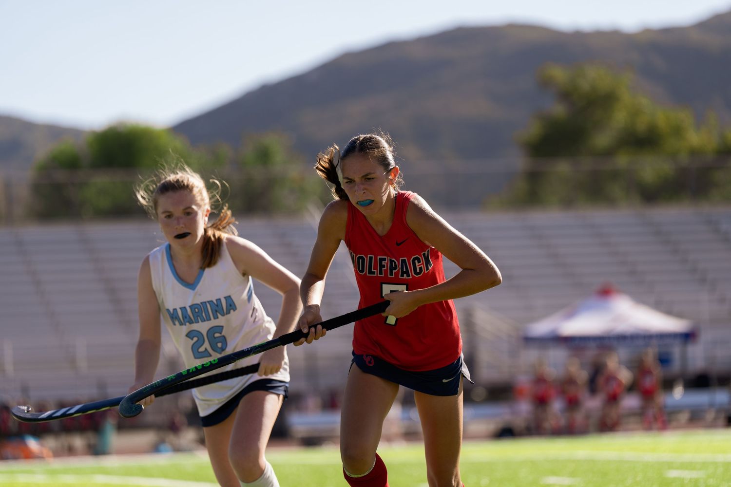 Athletes compete in a track and field event with mountains visible in the background on a sunny day.