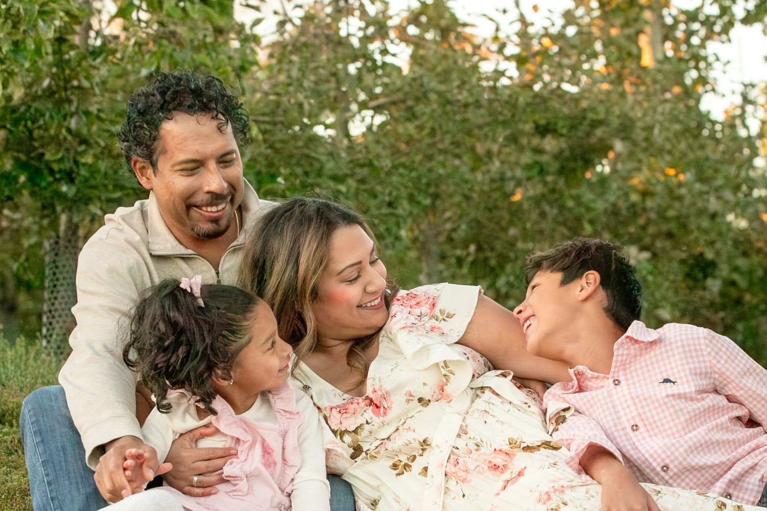 A family lounges together on grass during a warm autumn day with trees in the background.