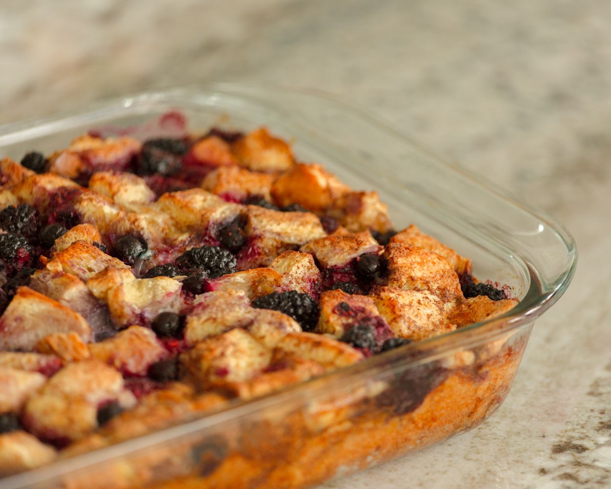 Golden baked berry bread pudding with blueberries and blackberries in a glass casserole dish.