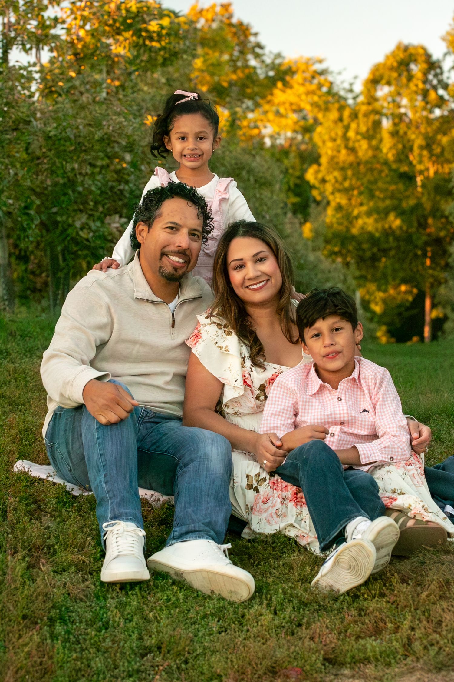 A family sits together on grass with beautiful fall foliage creating a golden backdrop in nature.