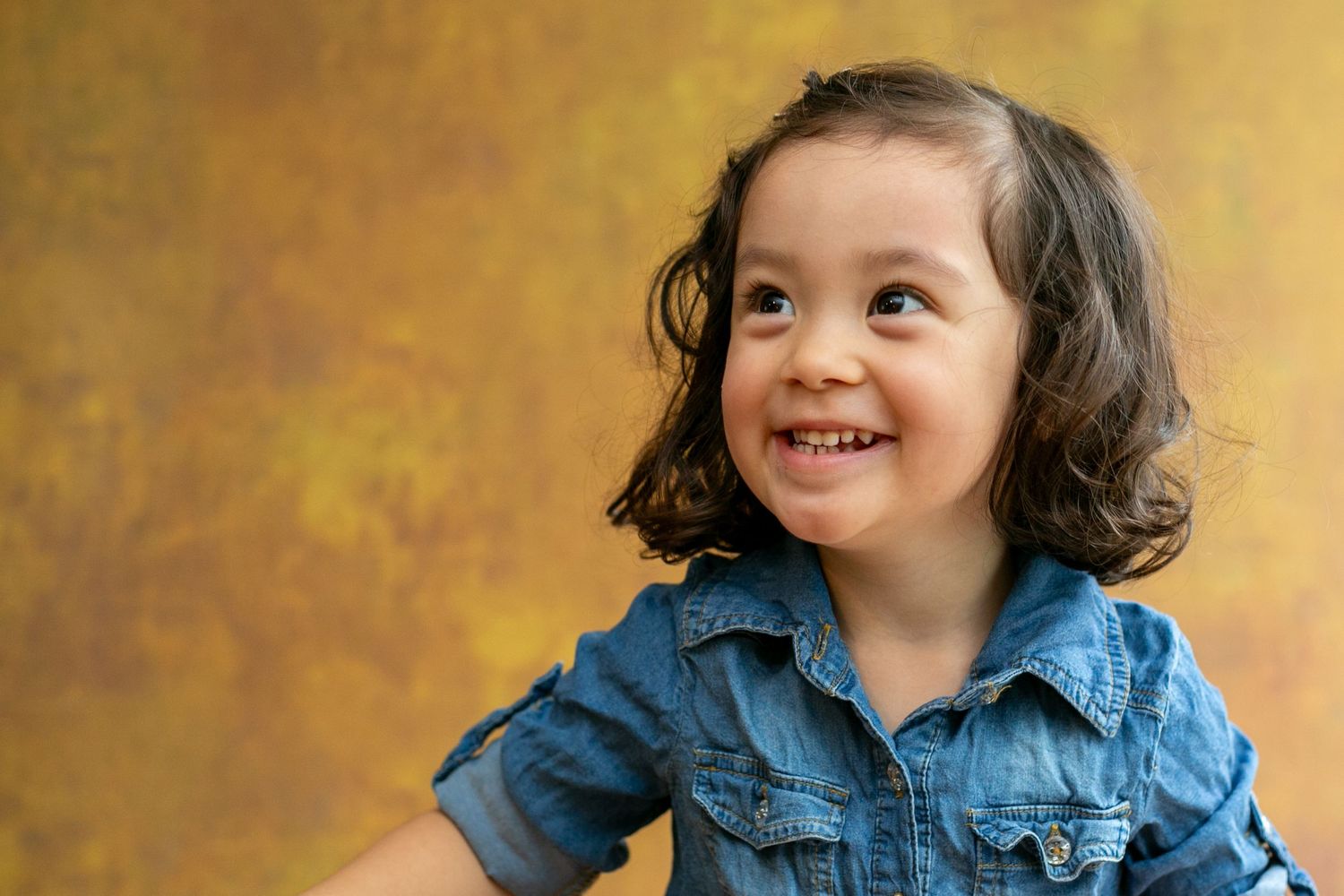 A sequence of photos showing a young child in a denim shirt making various playful facial expressions against a golden backdrop.