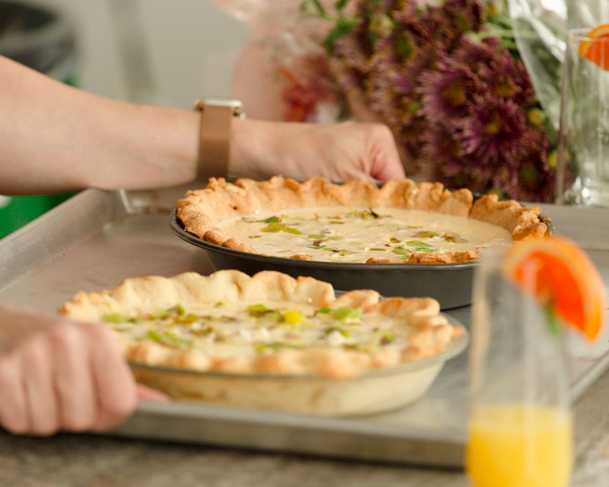 Two golden quiche pies with green onion topping on a baking sheet being prepared.