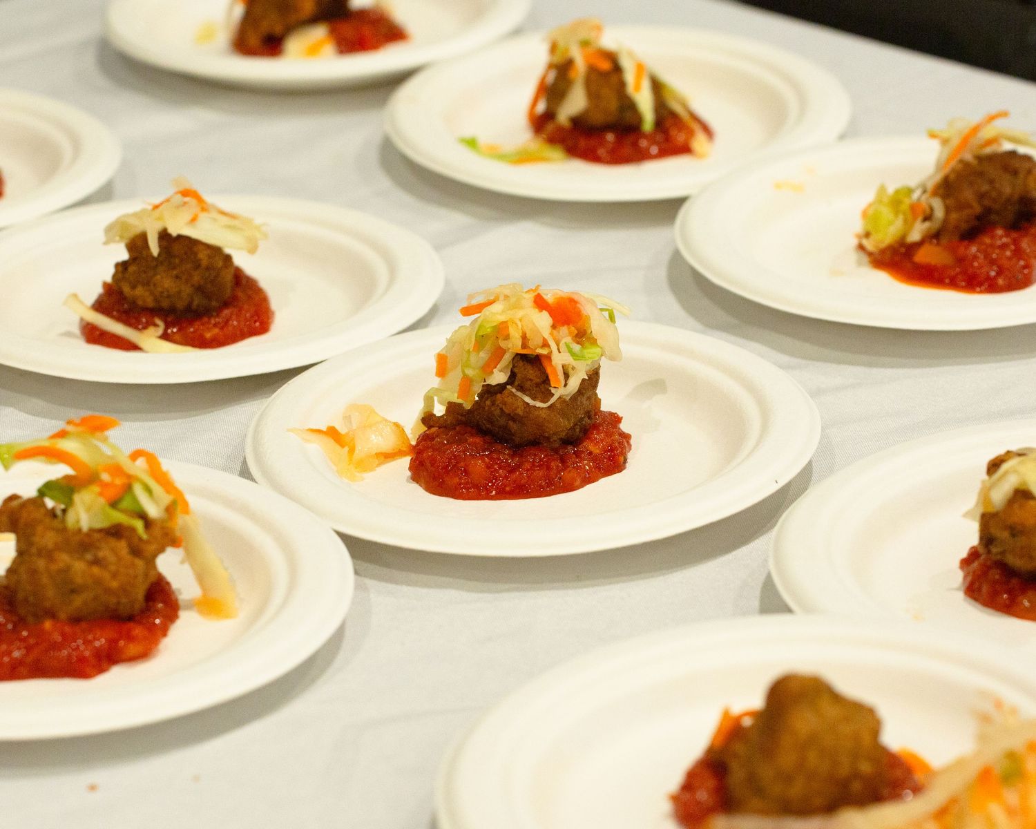 Elegant appetizer plates with meatballs on tomato sauce topped with fresh coleslaw, arranged for a catered event.
