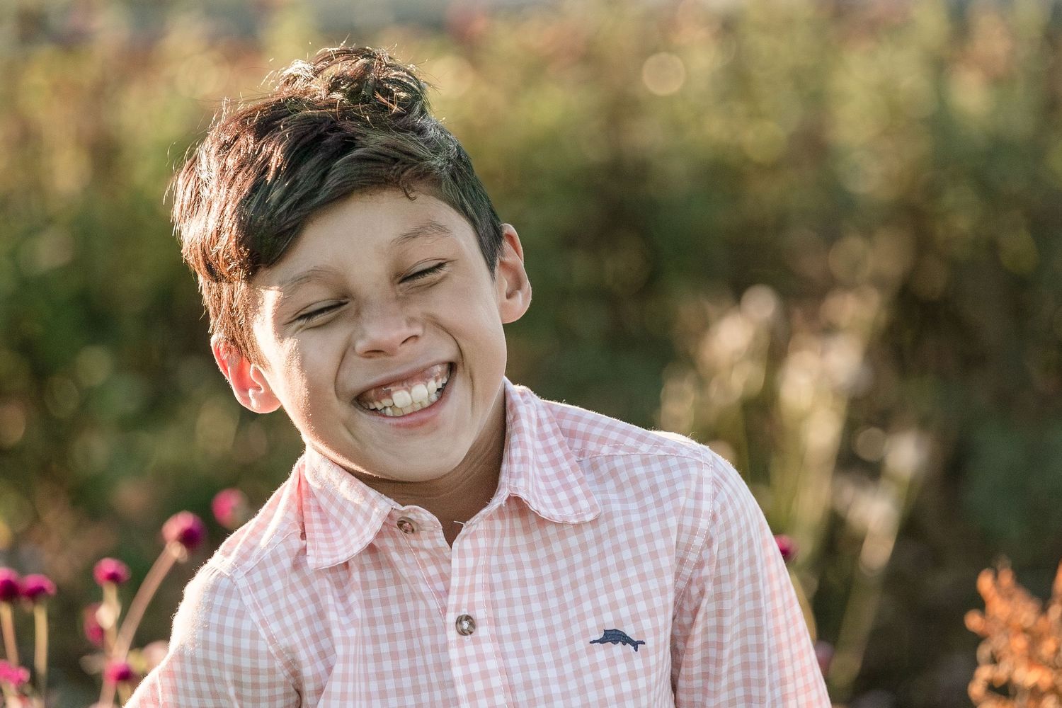 A joyful candid portrait in a pink gingham shirt against a soft bokeh garden background.