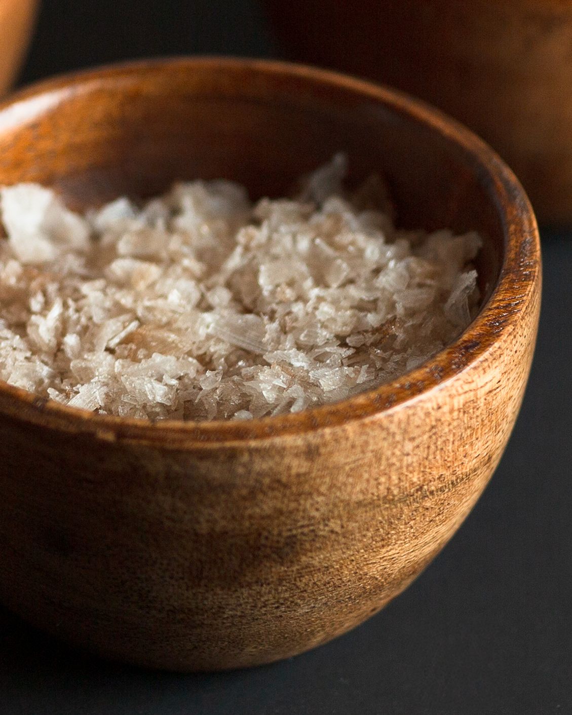 Flaky sea salt in a rustic wooden bowl on a dark background, perfect for gourmet cooking and seasoning.