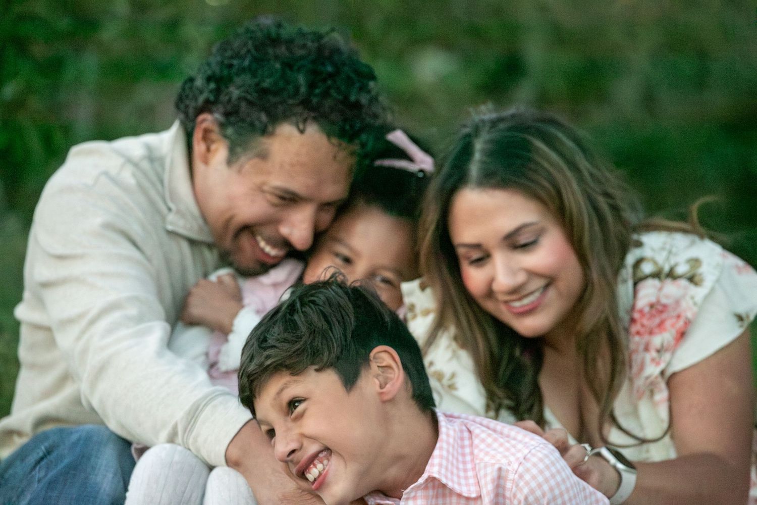 Happy family of four laughing and embracing outdoors, parents hugging children in a warm candid moment.