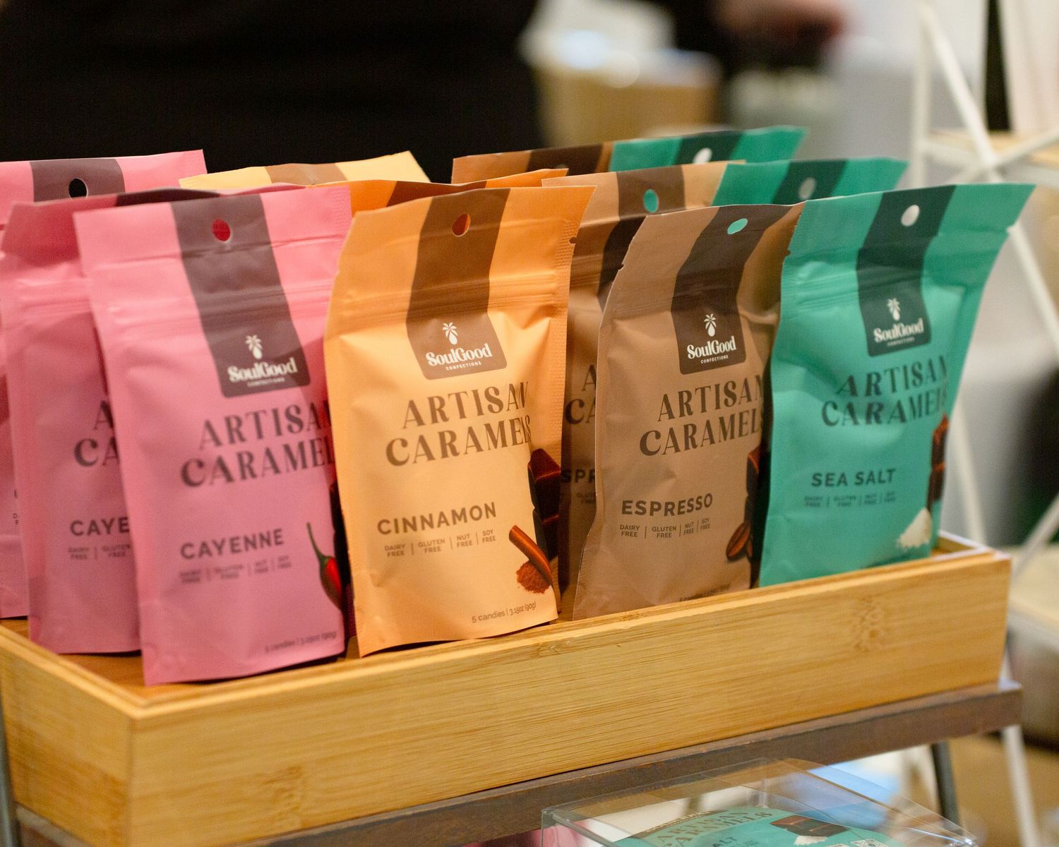 Assorted artisan caramel bags in pink, orange, and teal flavors including cayenne, cinnamon, espresso, and sea salt on display.