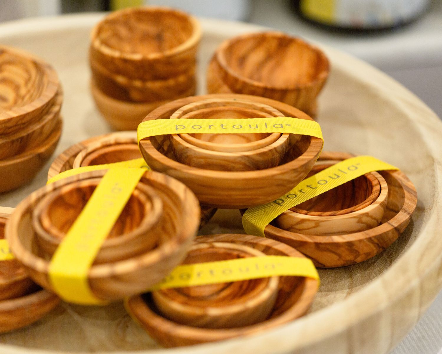 Handcrafted olive wood bowls with yellow branded ribbons displayed on a large wooden tray in a gift shop.