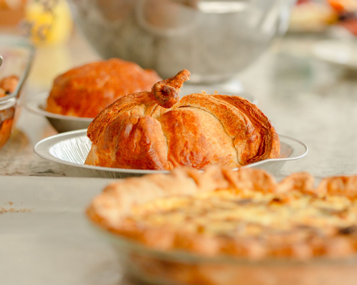 Golden roasted turkey on a white plate surrounded by Thanksgiving dishes including a pie on a festive table.