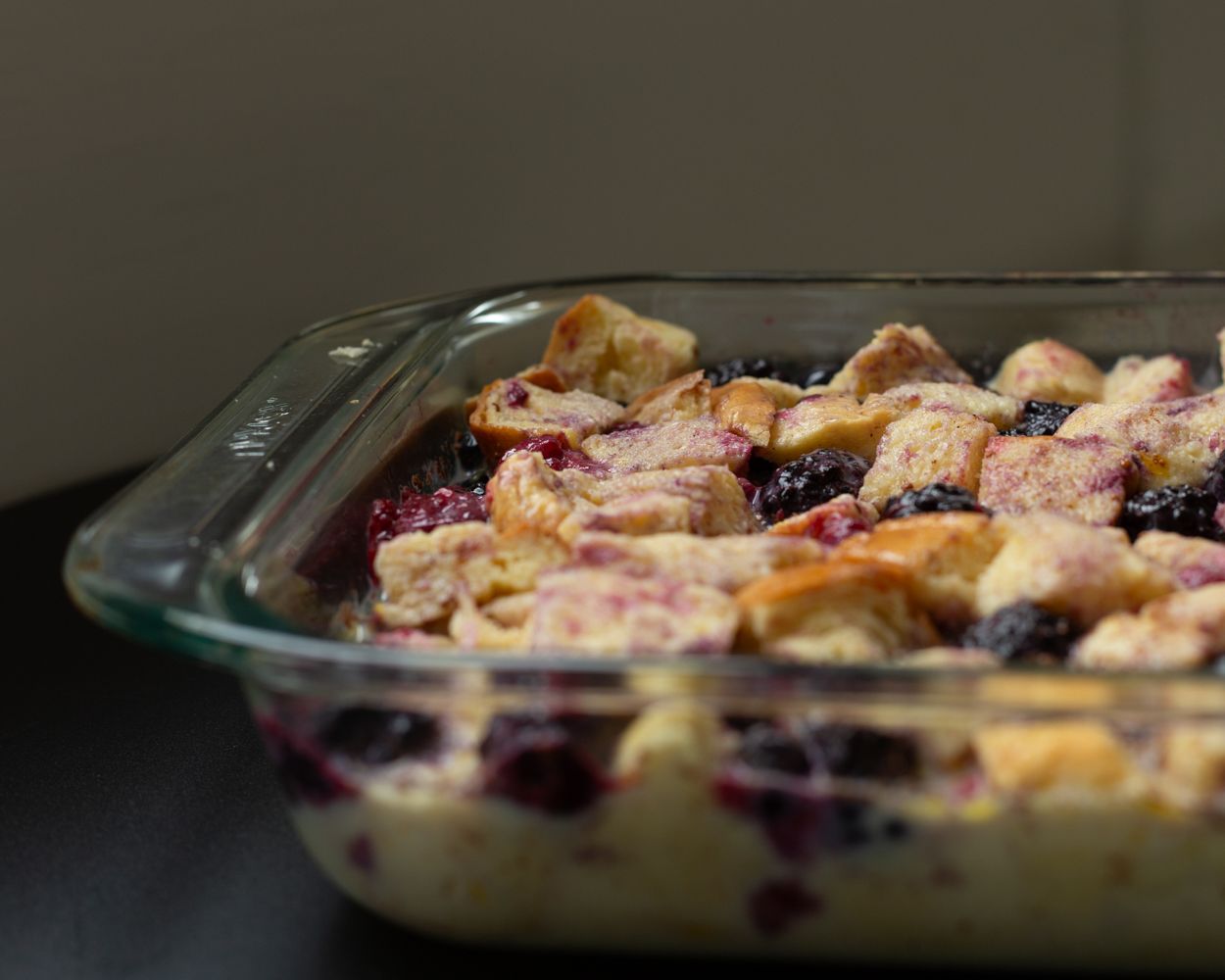 Glass baking dish filled with blueberry bread pudding, golden chunks of bread soaked in creamy custard with fresh berries.