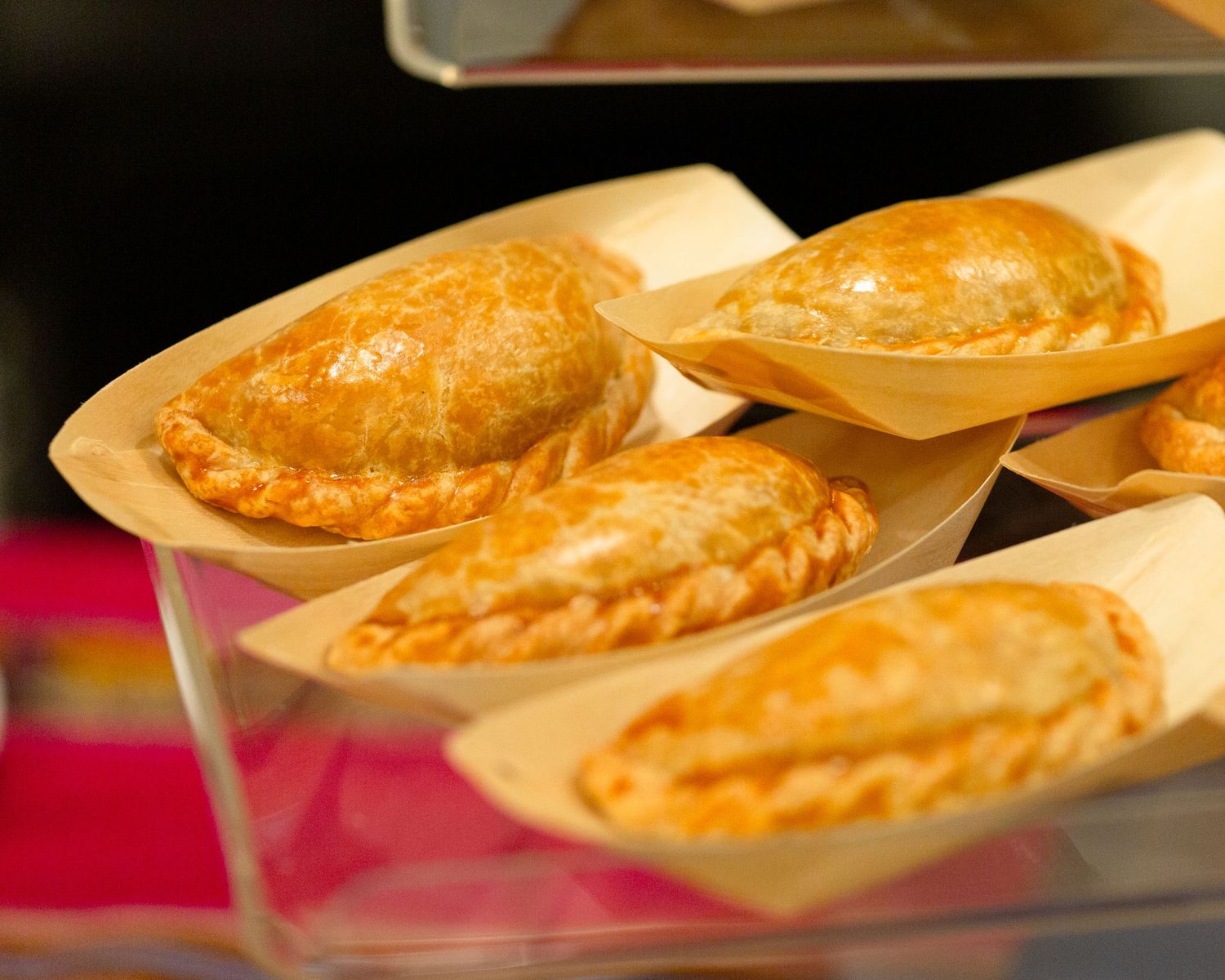 Golden baked empanadas served in wooden boat-shaped trays displayed in a glass case at a food market.