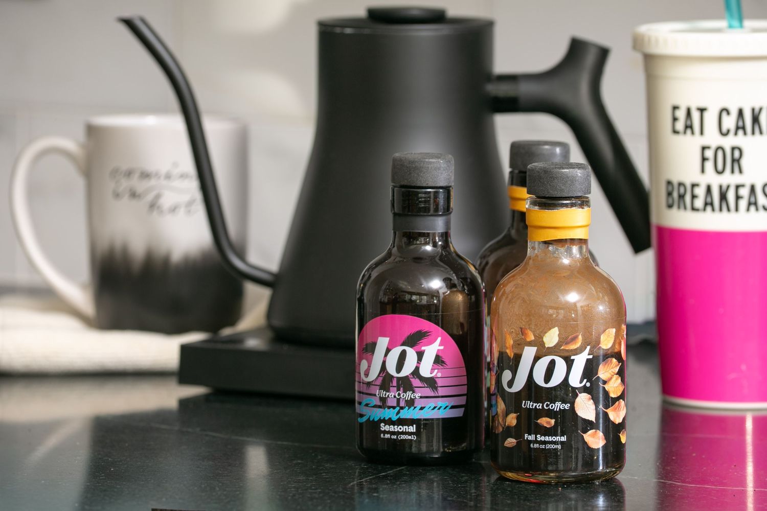 Two Jot ultra coffee concentrate bottles displayed on a counter with a gooseneck kettle and an Eat Cake For Breakfast cup.