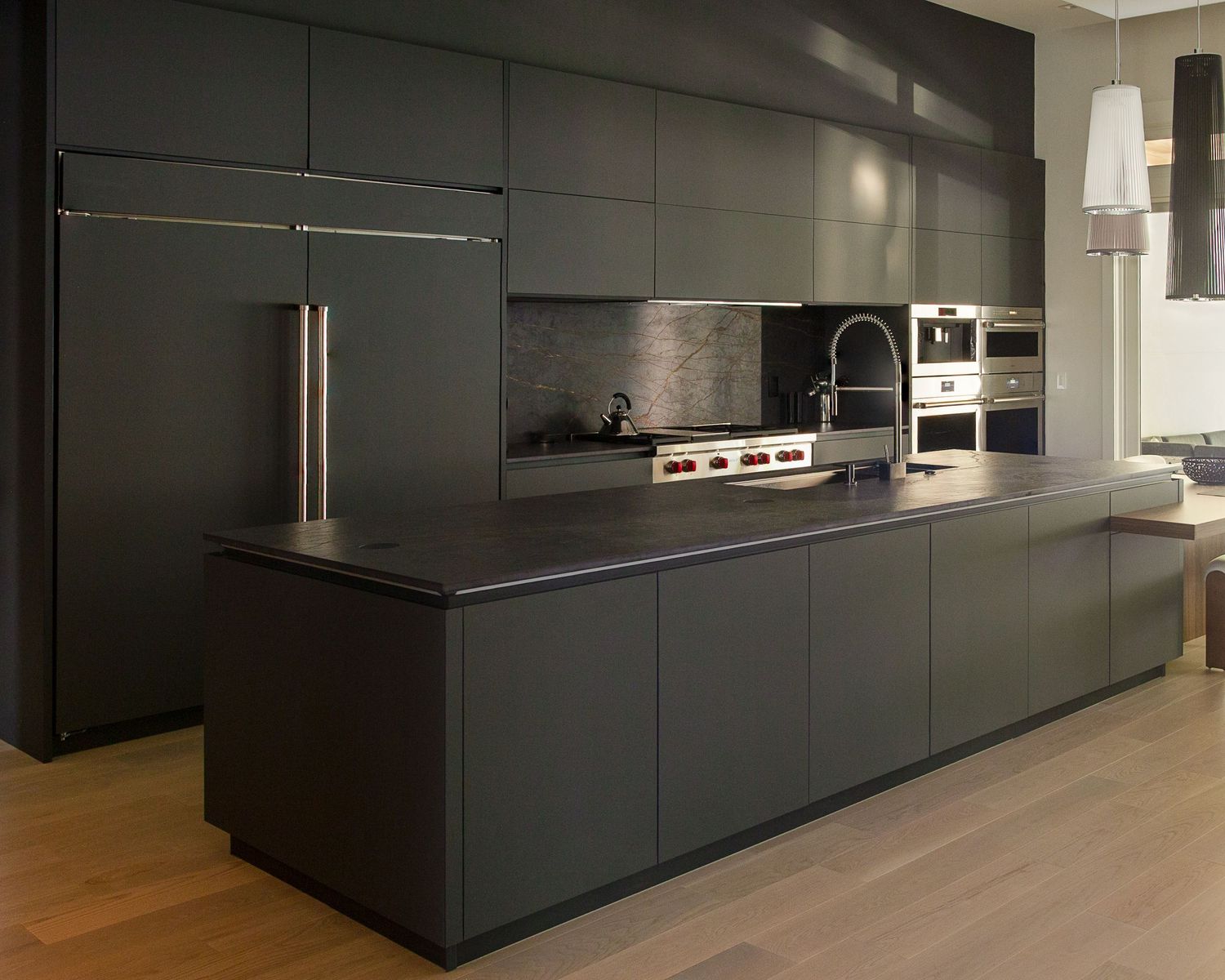 Modern black kitchen cabinets with sleek hardware extend along a minimalist interior with wood flooring.
