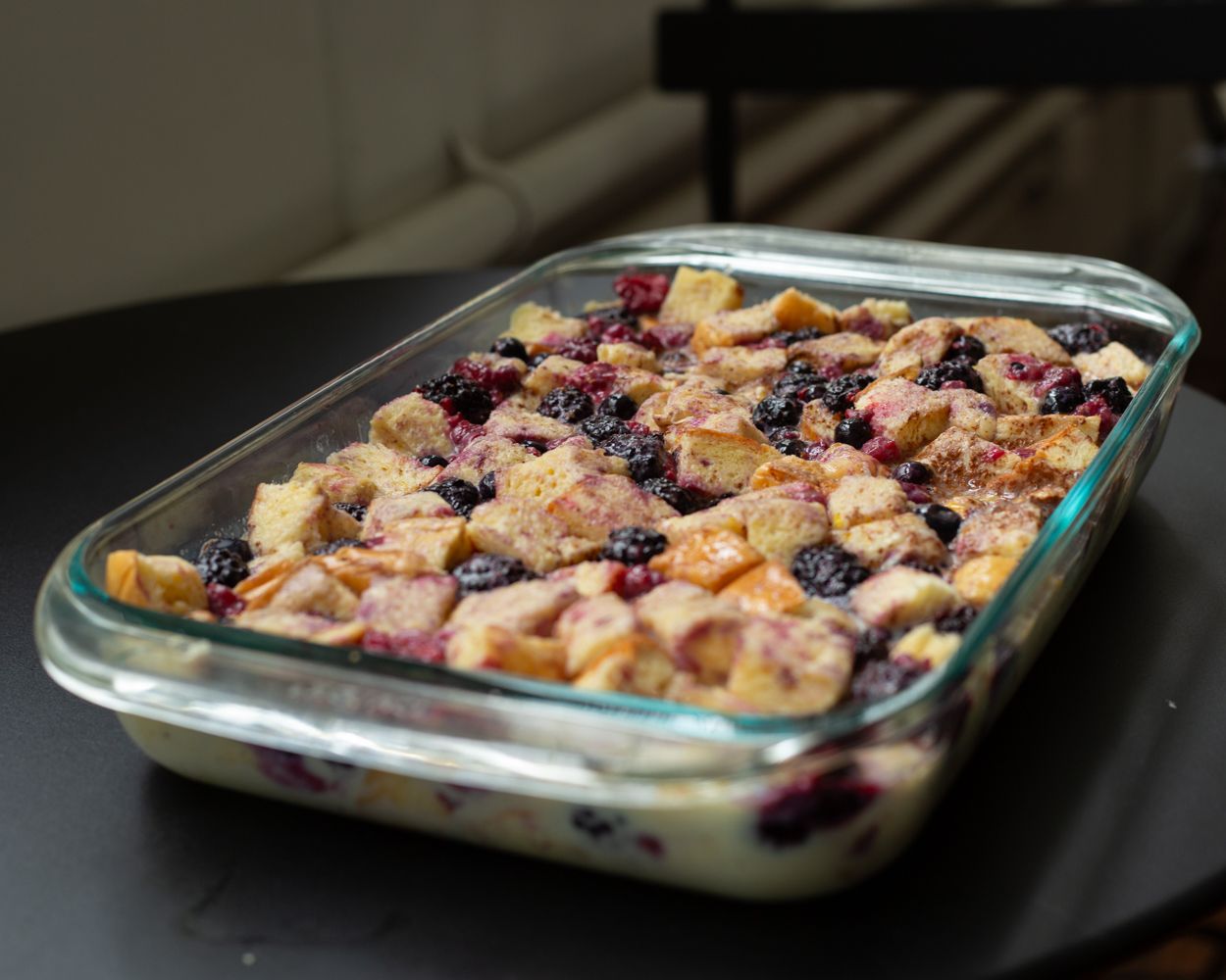 Glass baking dish filled with blueberry bread pudding, golden-brown cubes soaked in creamy custard with fresh berries.