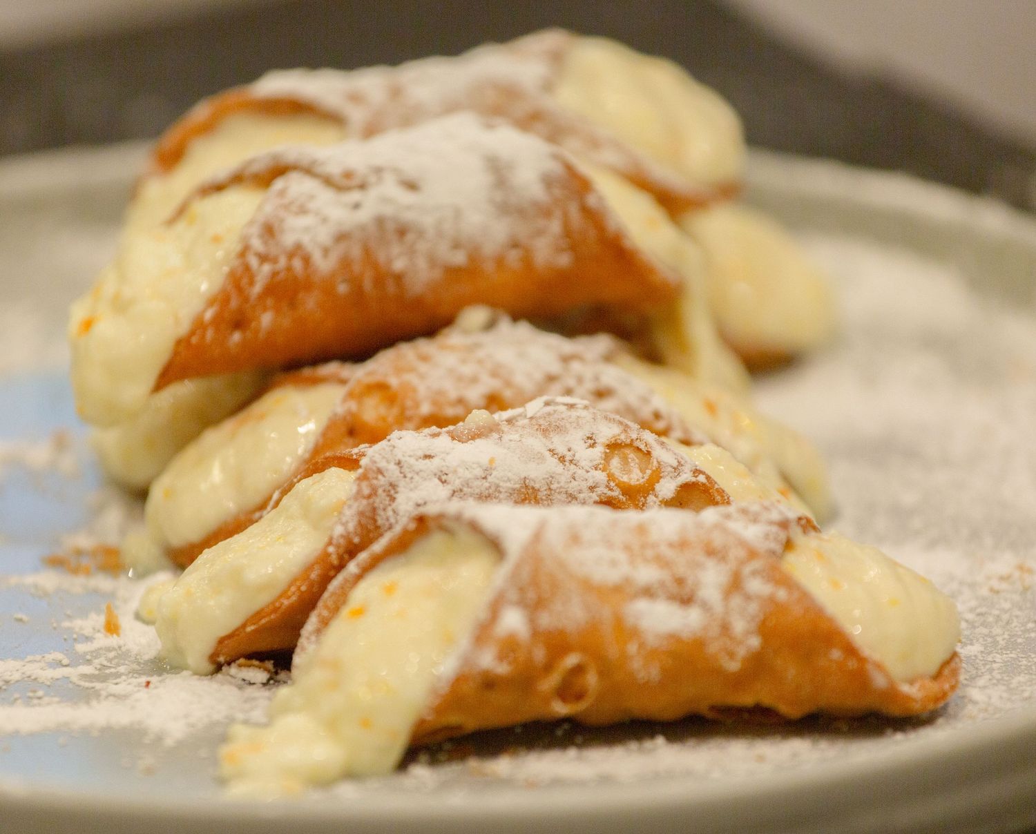 Golden pastry triangles dusted with powdered sugar and filled with creamy vanilla custard on a ceramic plate.