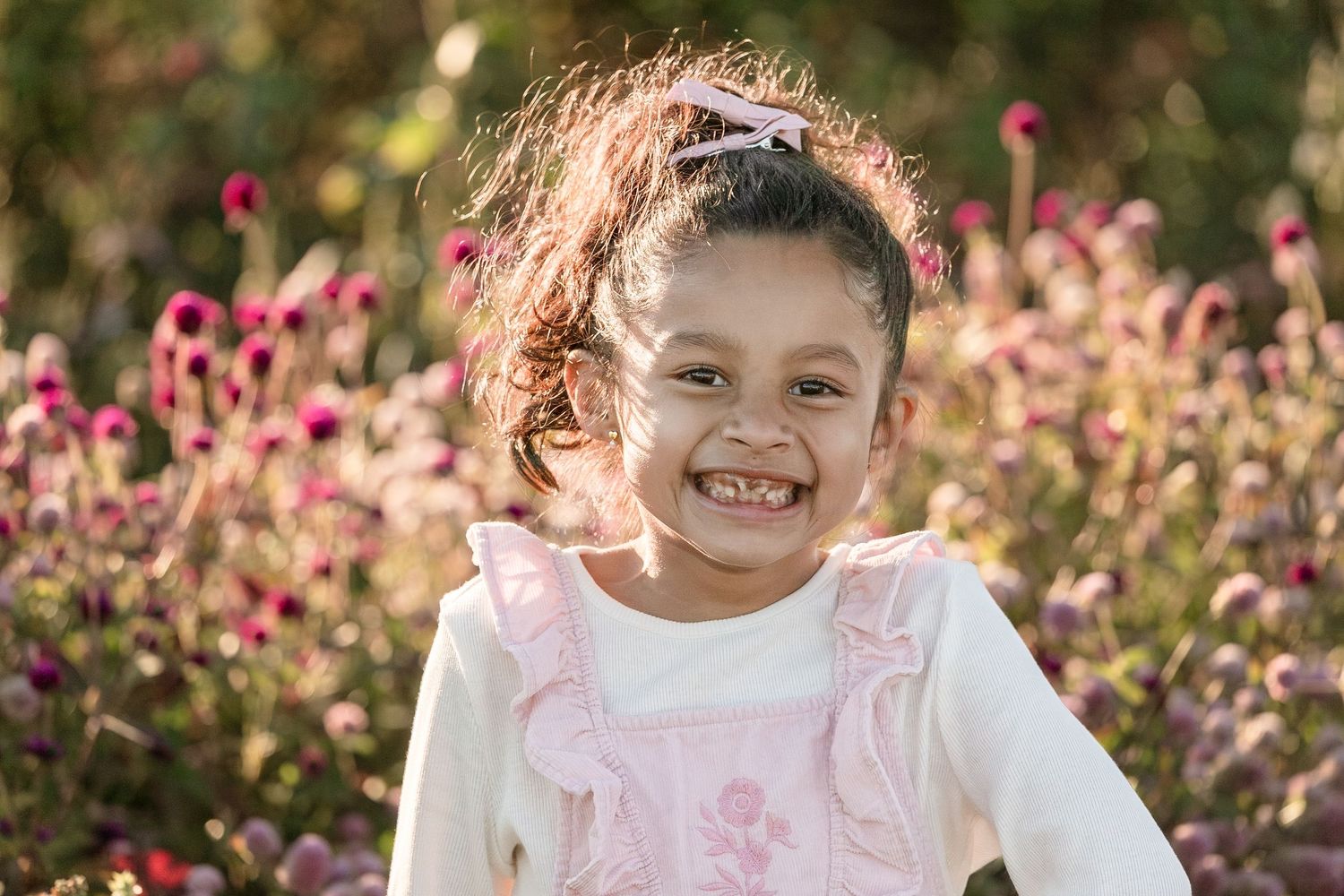 A bright natural light portrait with pink flowers and warm sunlight in the background.