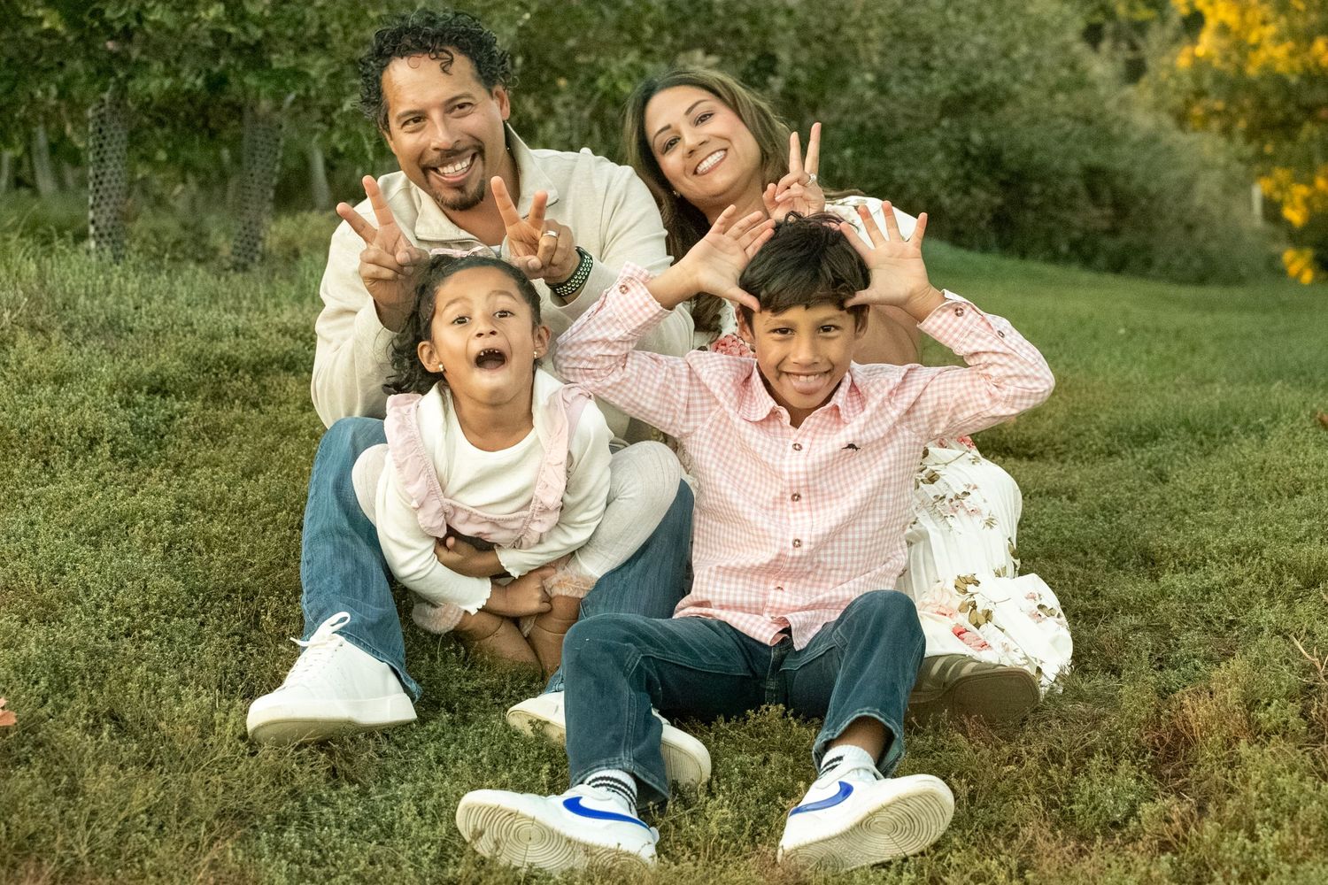 A family sits together on grass during a warm autumn day in a park setting.