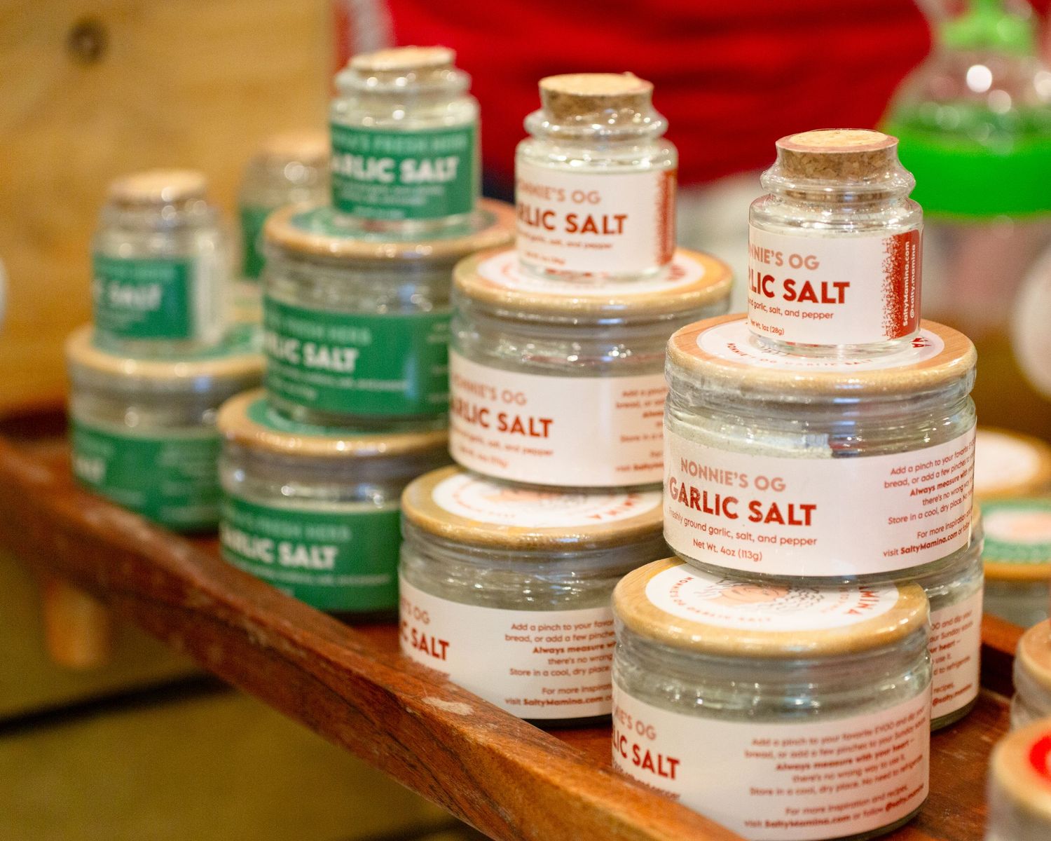 Multiple jars of artisan garlic salt seasoning displayed on a wooden shelf in a specialty food store.