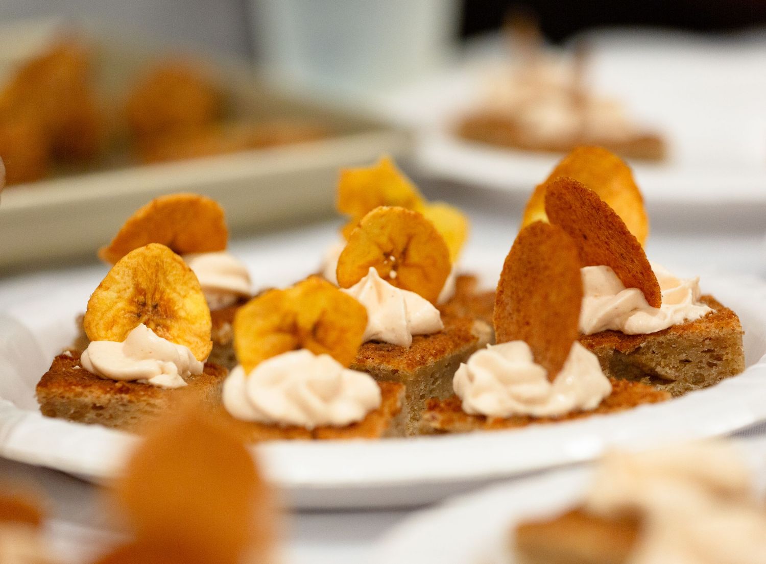 Bruschetta topped with whipped cream and crispy plantain chips served on a white plate.