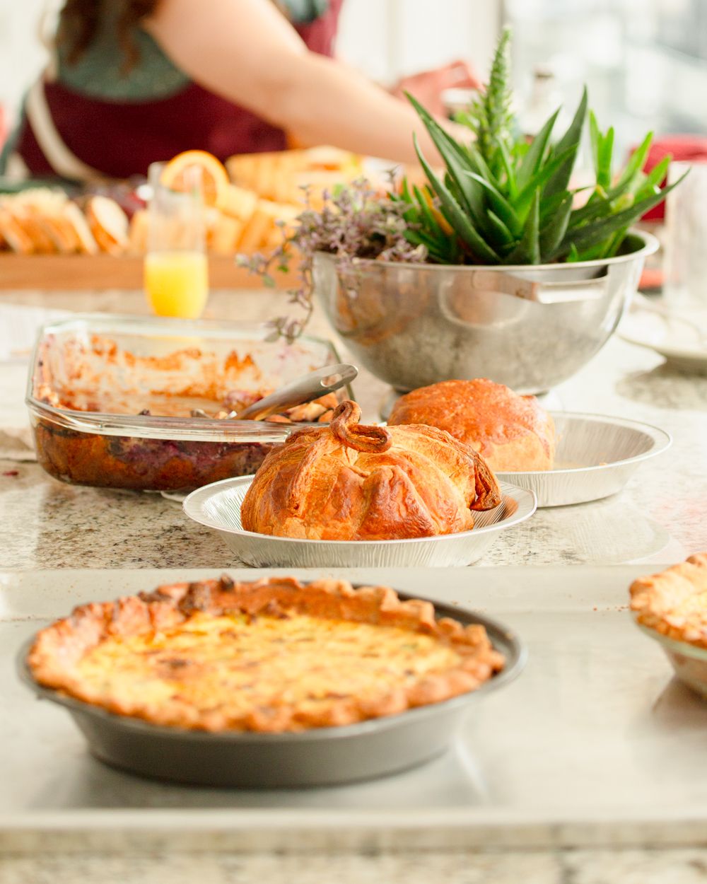 Spread of homemade baked goods including quiche, pastries, and casserole on a marble kitchen counter.