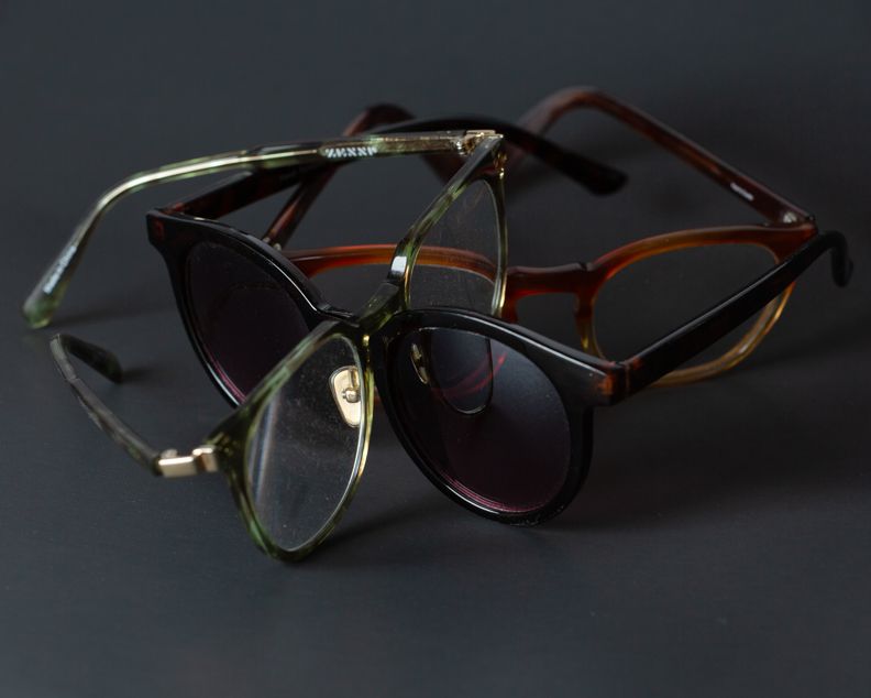 Three stylish eyeglass frames in tortoise, black, and green acetate arranged together on a dark background.