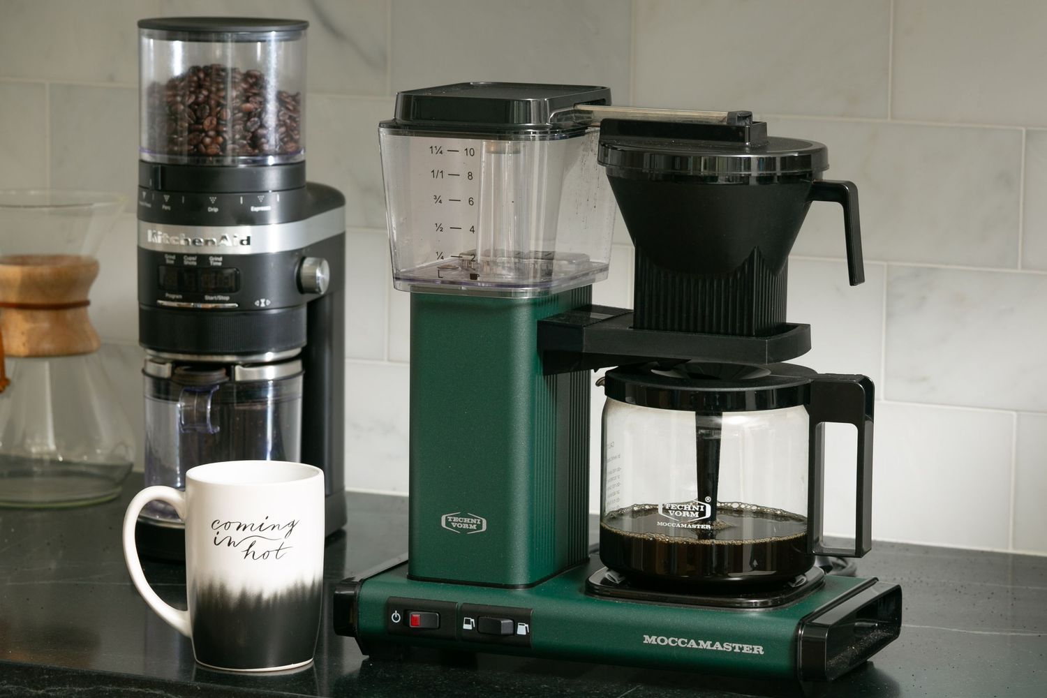 A series of coffee brewing equipment including grinders, pour-over drippers, and carafes arranged on a kitchen counter.