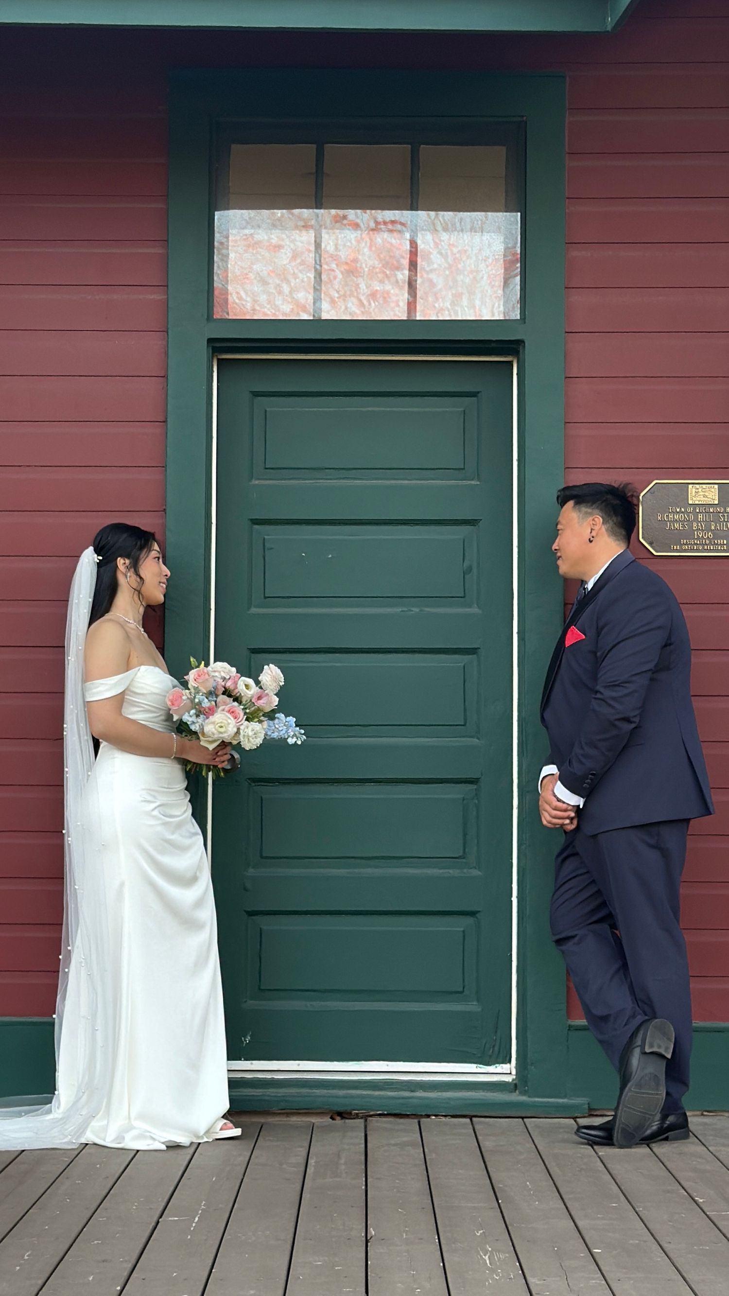 Wedding couple posing in front of green door on rustic red building.