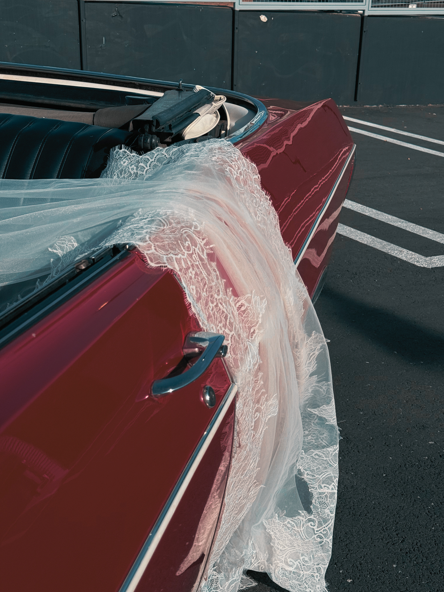 Red vintage car decorated with flowing white lace fabric in a parking lot.