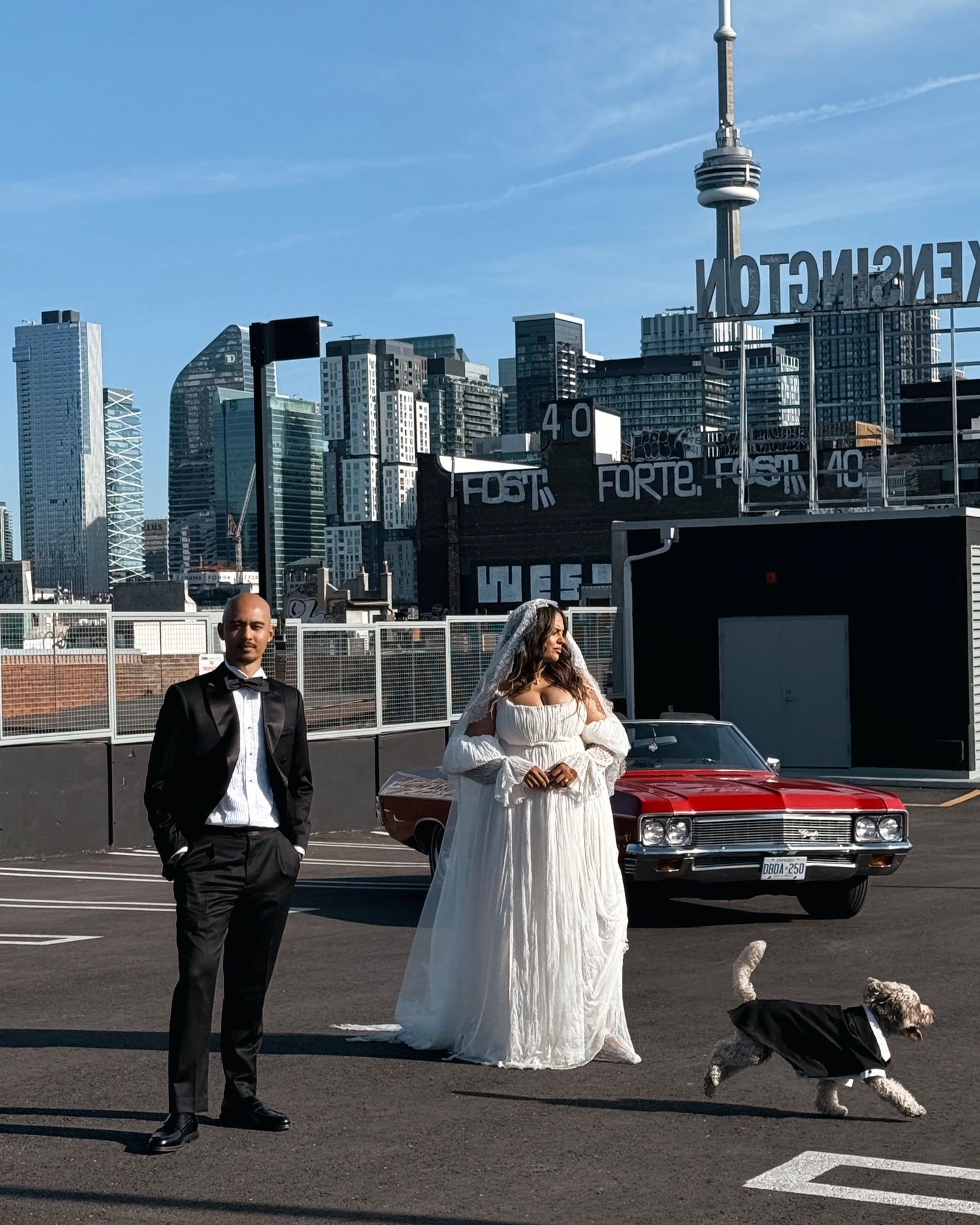 Wedding photo against Toronto skyline with CN Tower and classic red car.