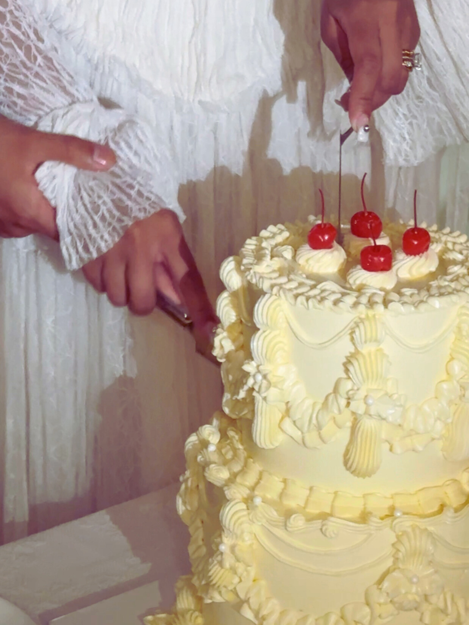Yellow frosted wedding cake being decorated with red cherries on top.