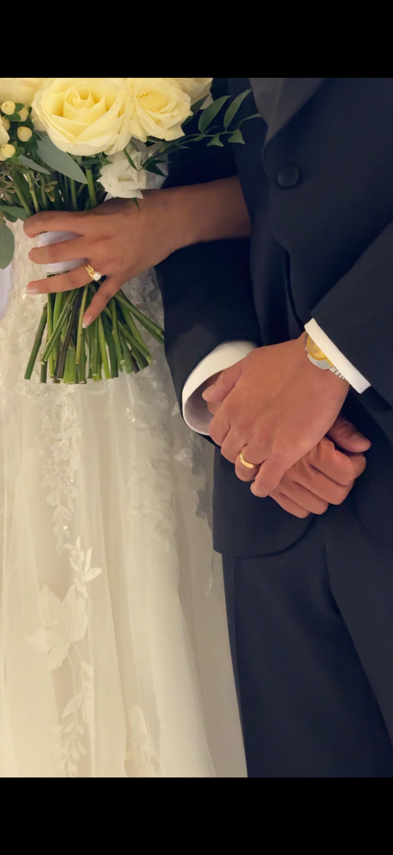 Close-up of wedding couple's hands holding white rose bouquet against black suit and white dress.