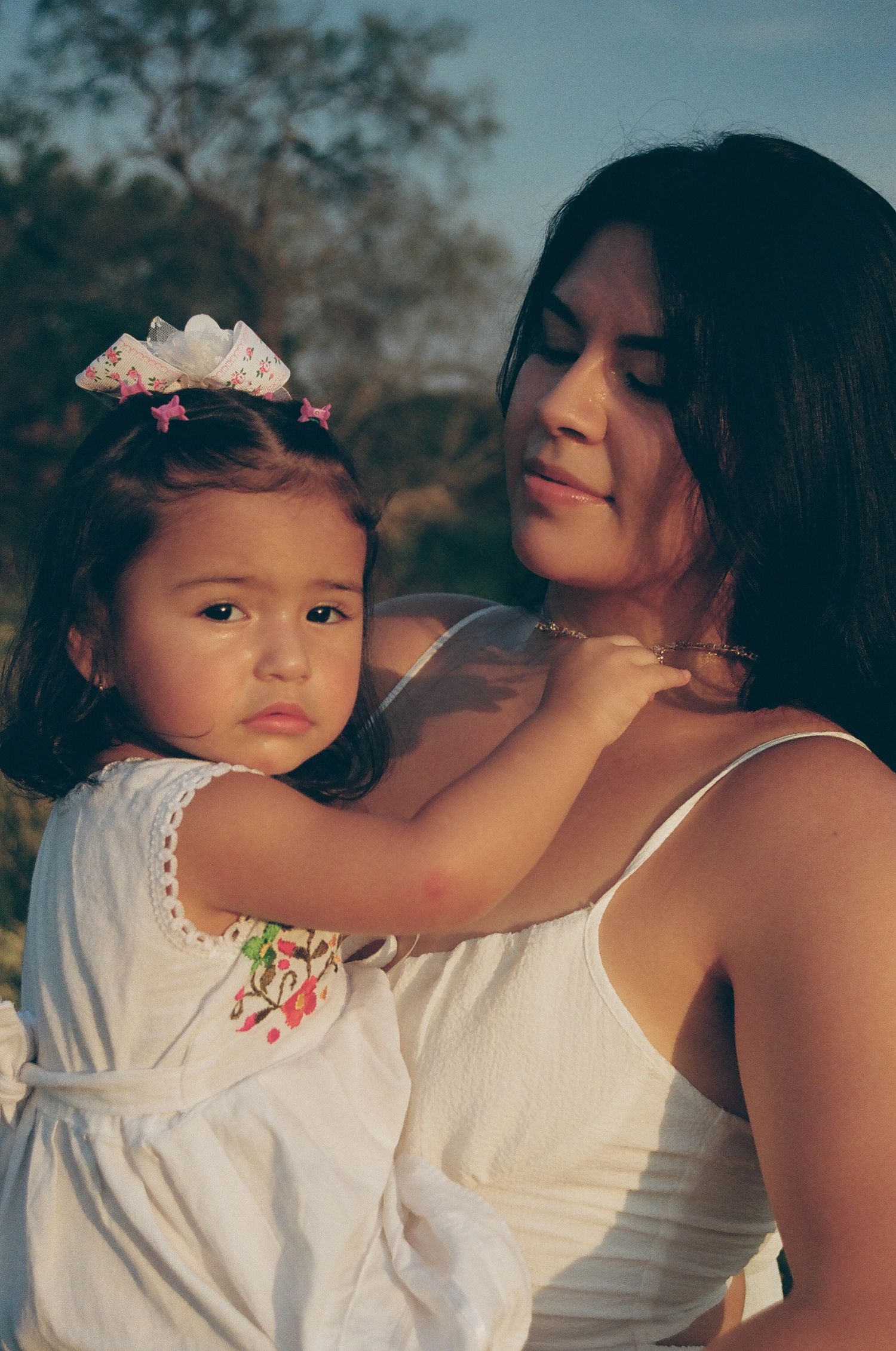 A tender moment captured in white clothing against a natural outdoor setting during golden hour.
