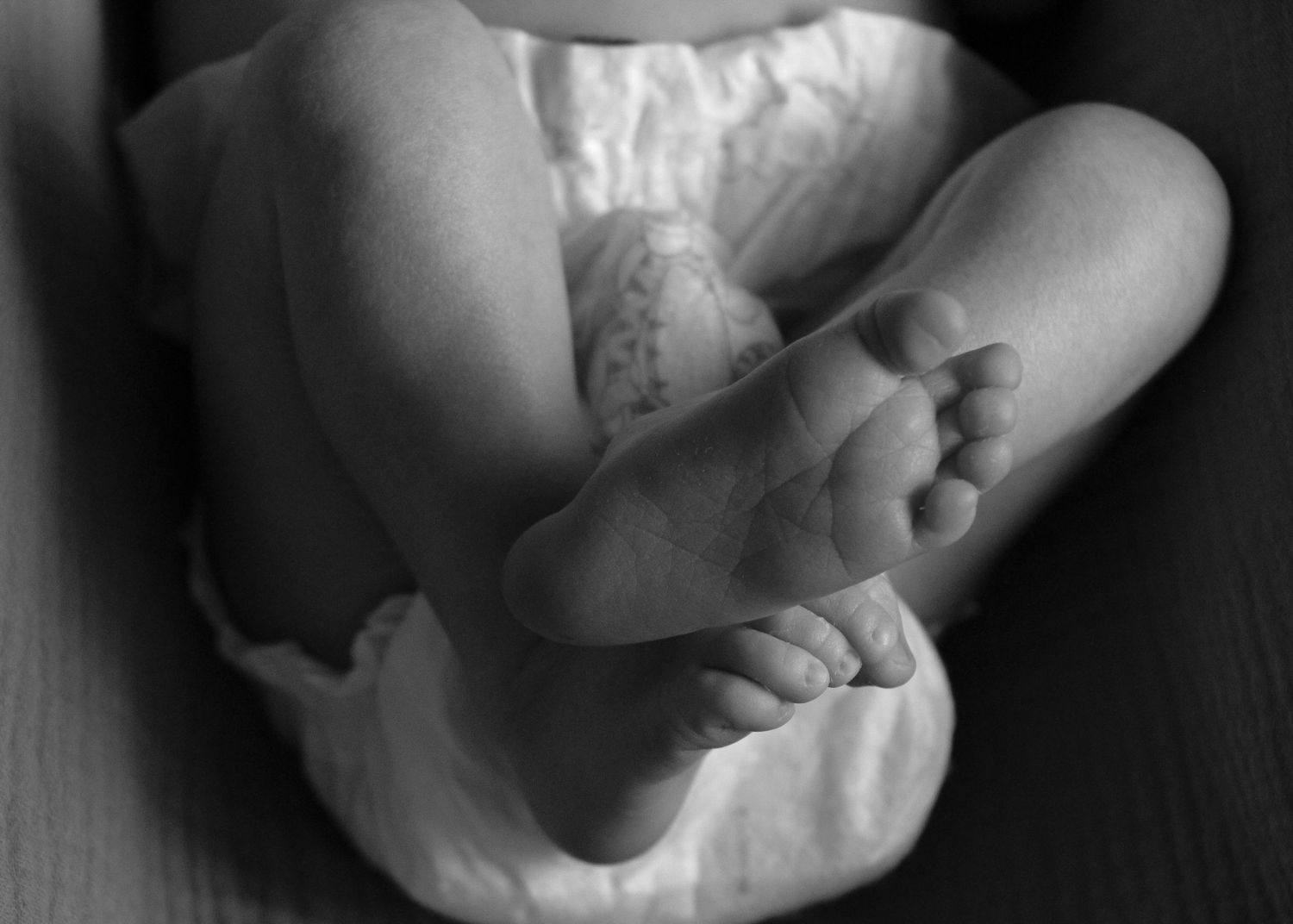 Black and white artistic photograph of a baby's tiny hand grasping an adult finger in a tender moment.
