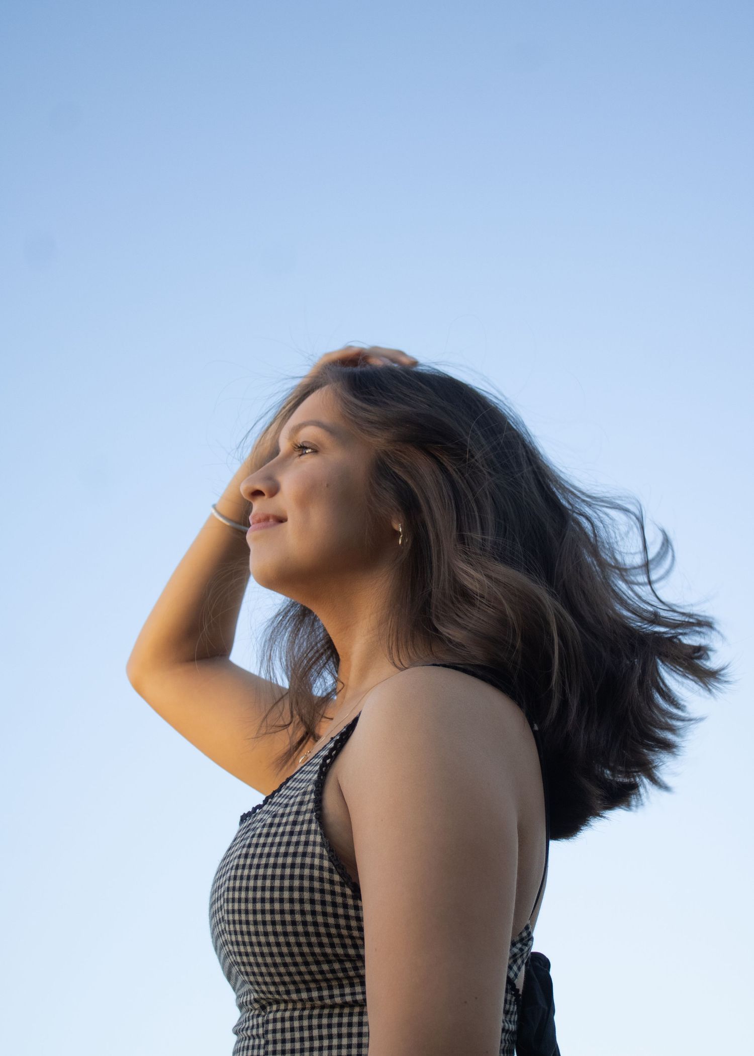 A figure in a checkered top poses dynamically against a blue sky with flowing hair in a sequence of motion shots.