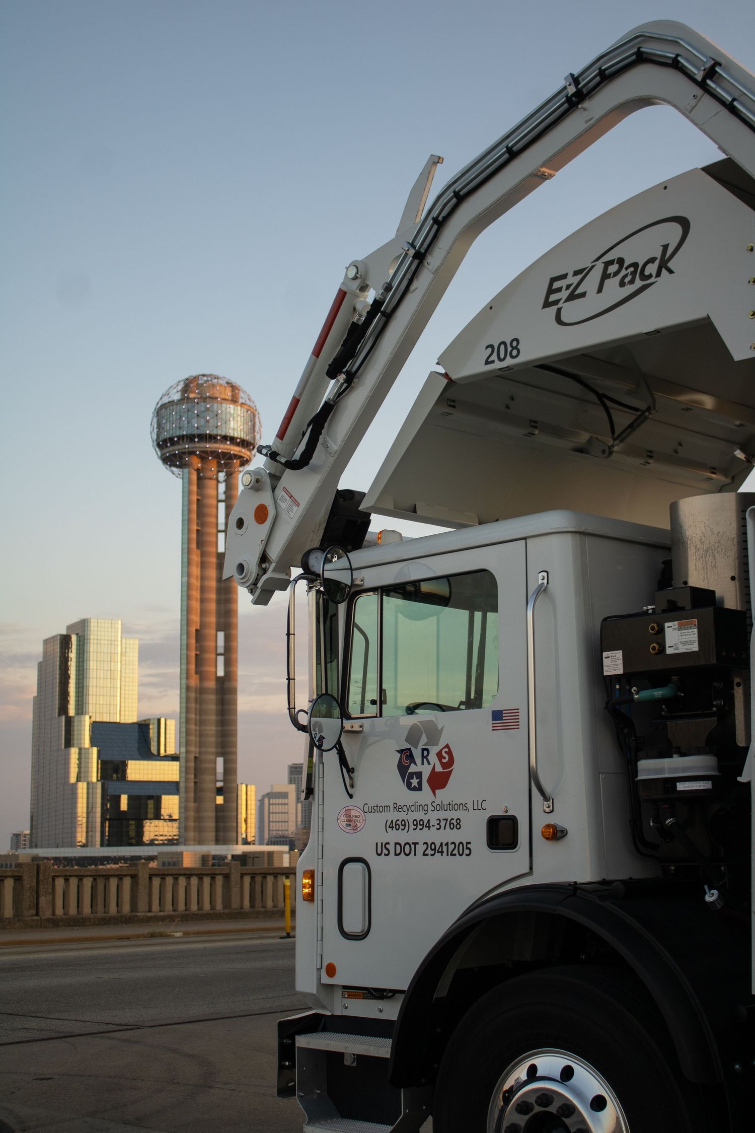Garbage truck parked with Reunion Tower landmark visible in downtown Dallas skyline.