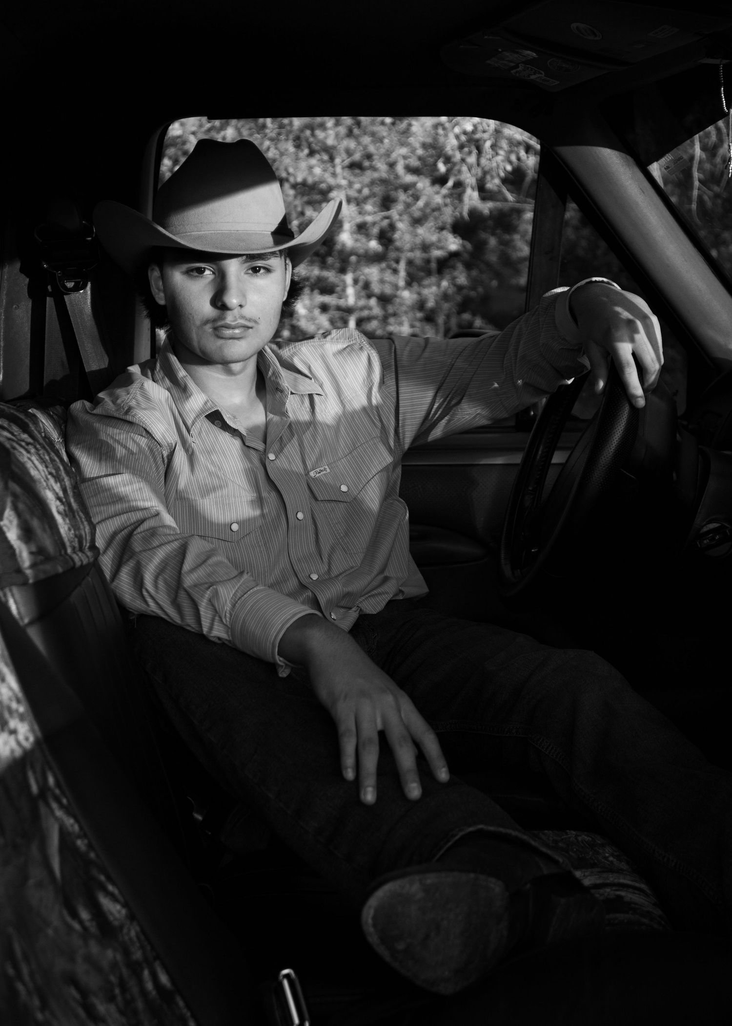 Young man in cowboy hat sitting in truck driver seat, black and white portrait photography.