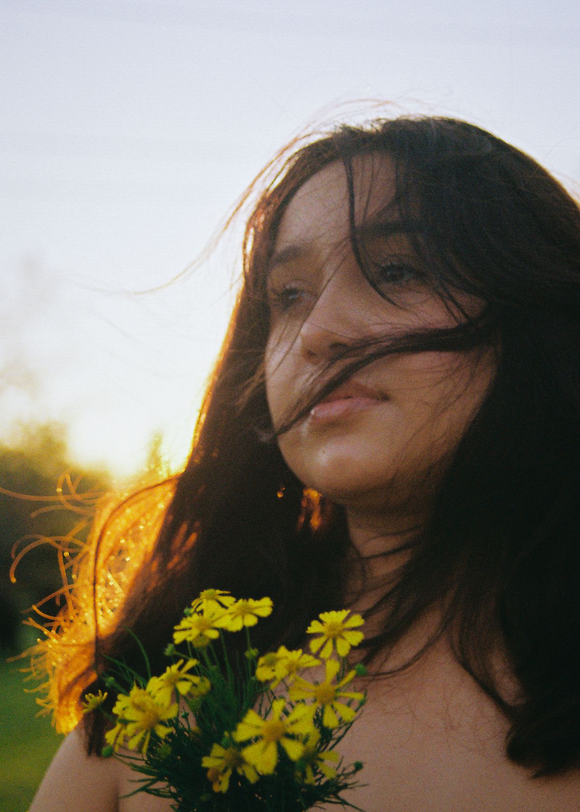 Woman posing with yellow daisies in golden sunlight creating a dreamy outdoor portrait.