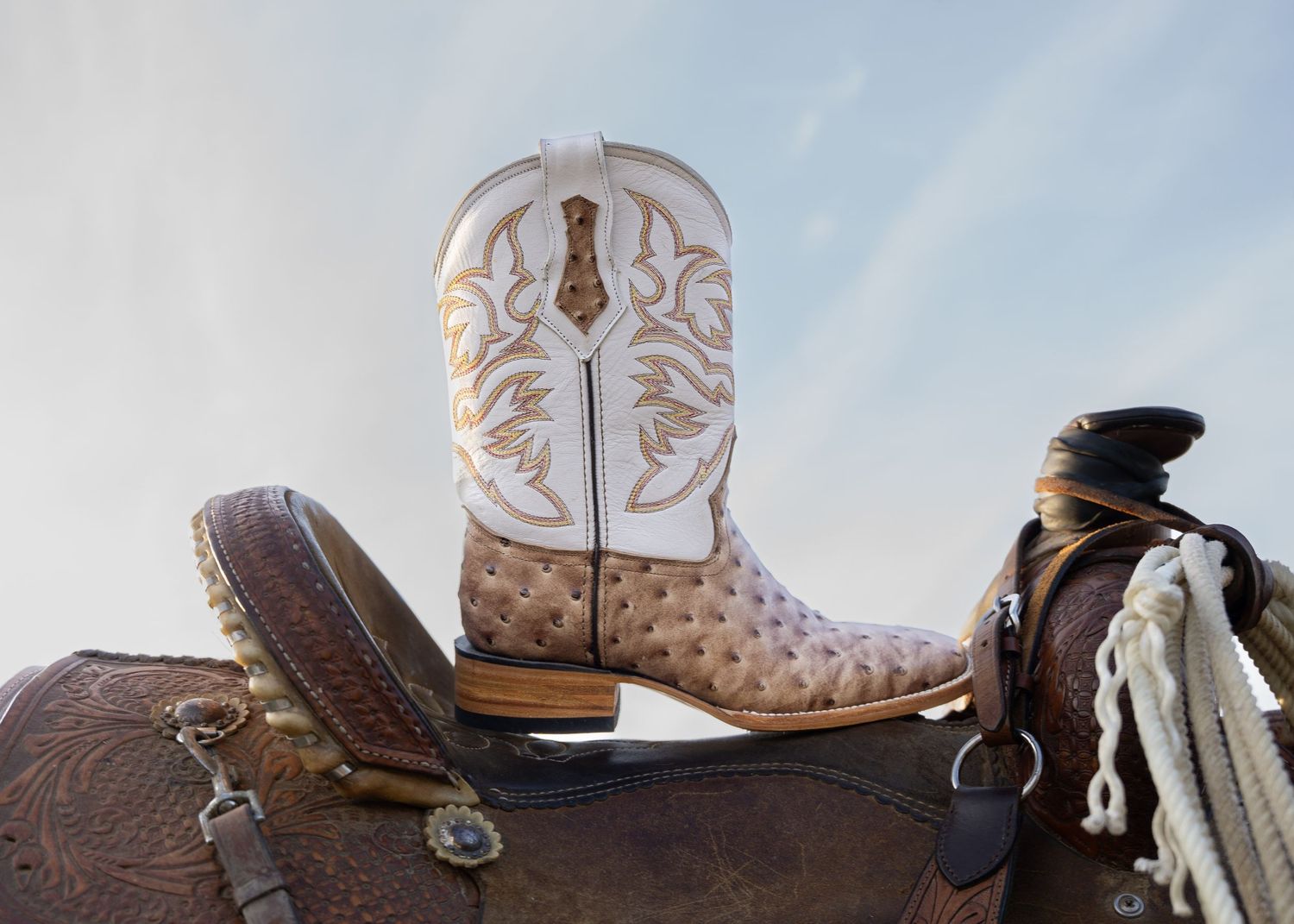 Close-up view of white leather cowboy boots with intricate stitching and decorative patterns on display.