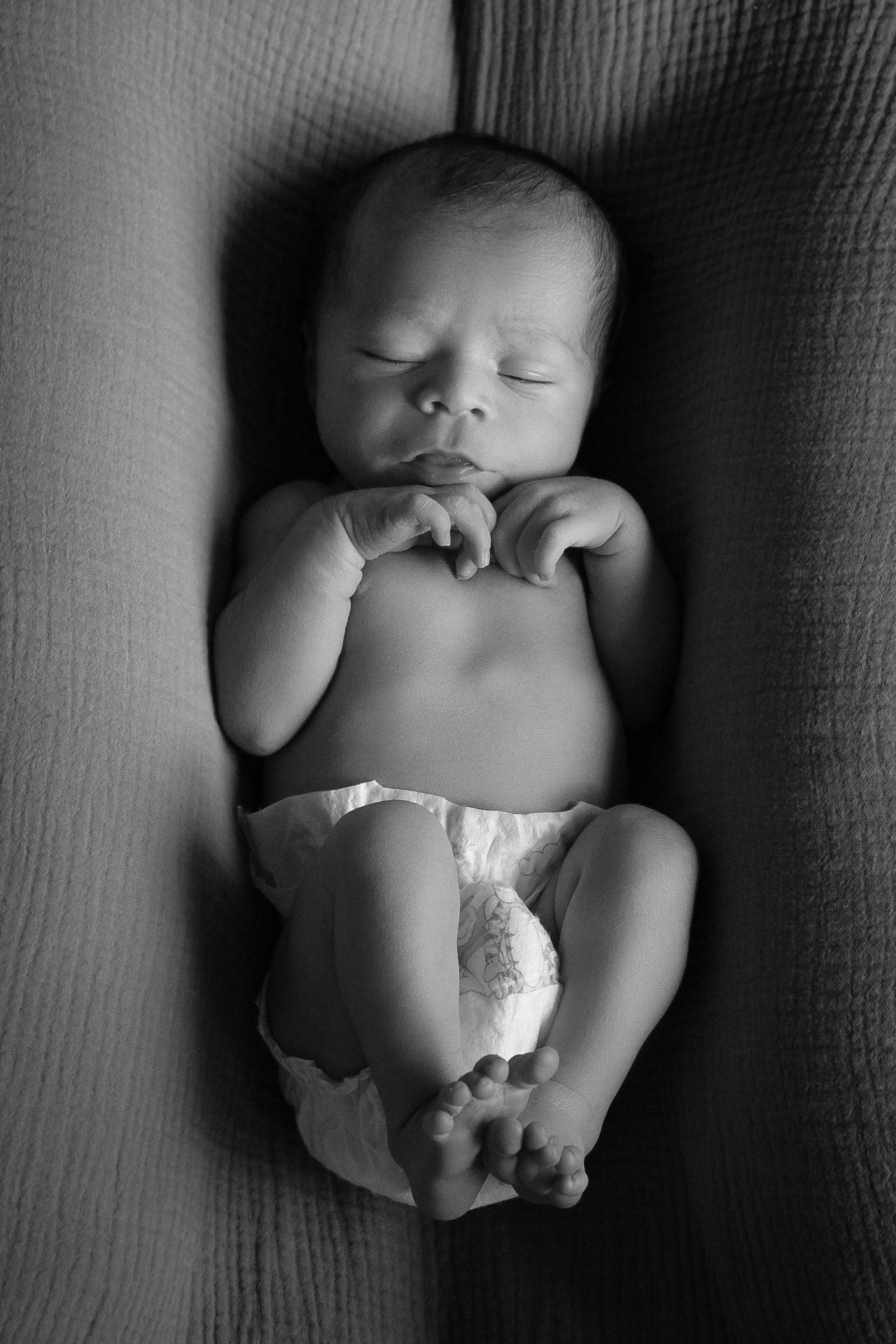 Black and white portrait of a sleeping newborn baby on textured fabric.