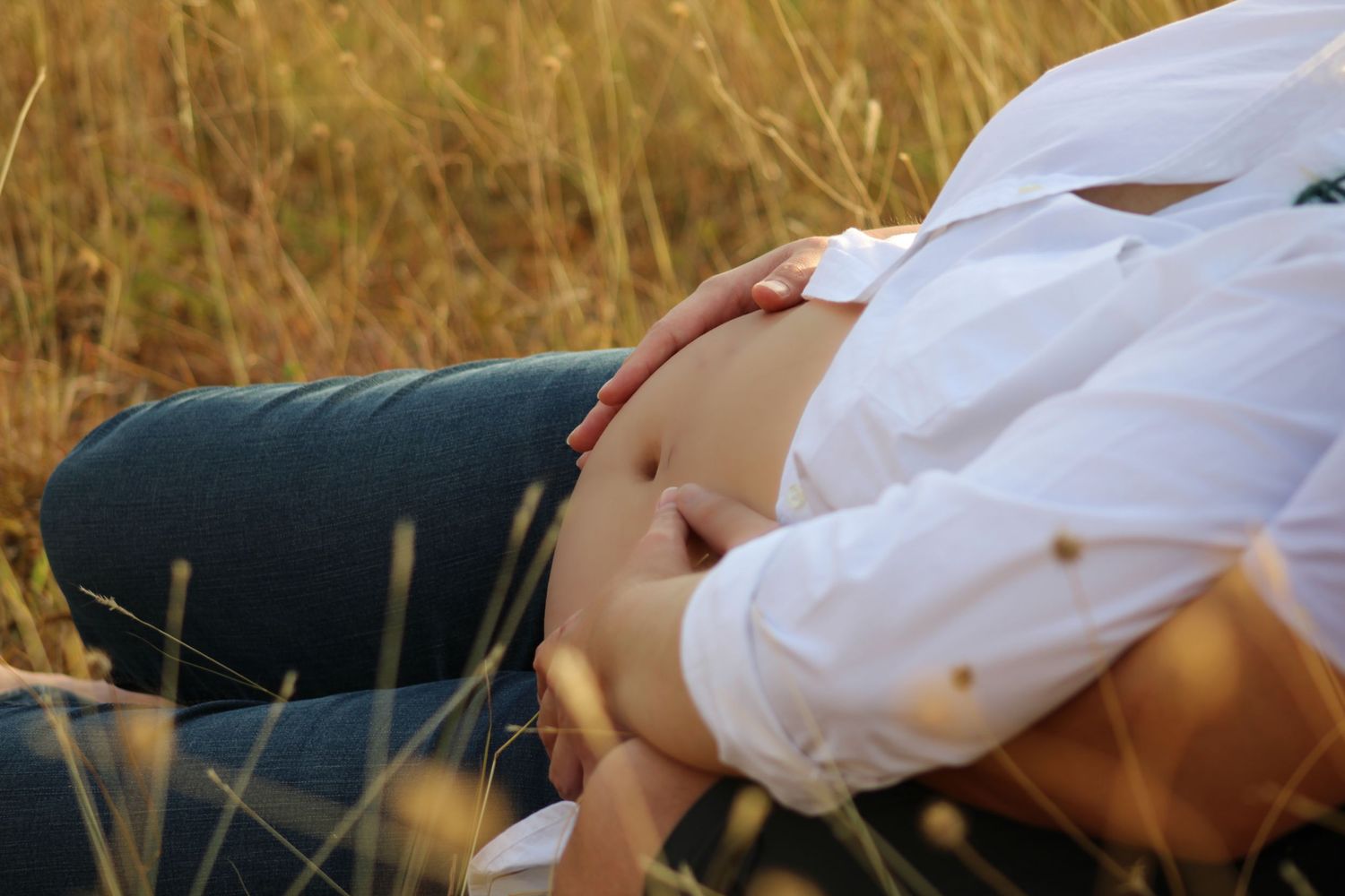 Person lying in a field of tall golden grass wearing a white shirt with sunlight creating a warm, dreamy atmosphere.