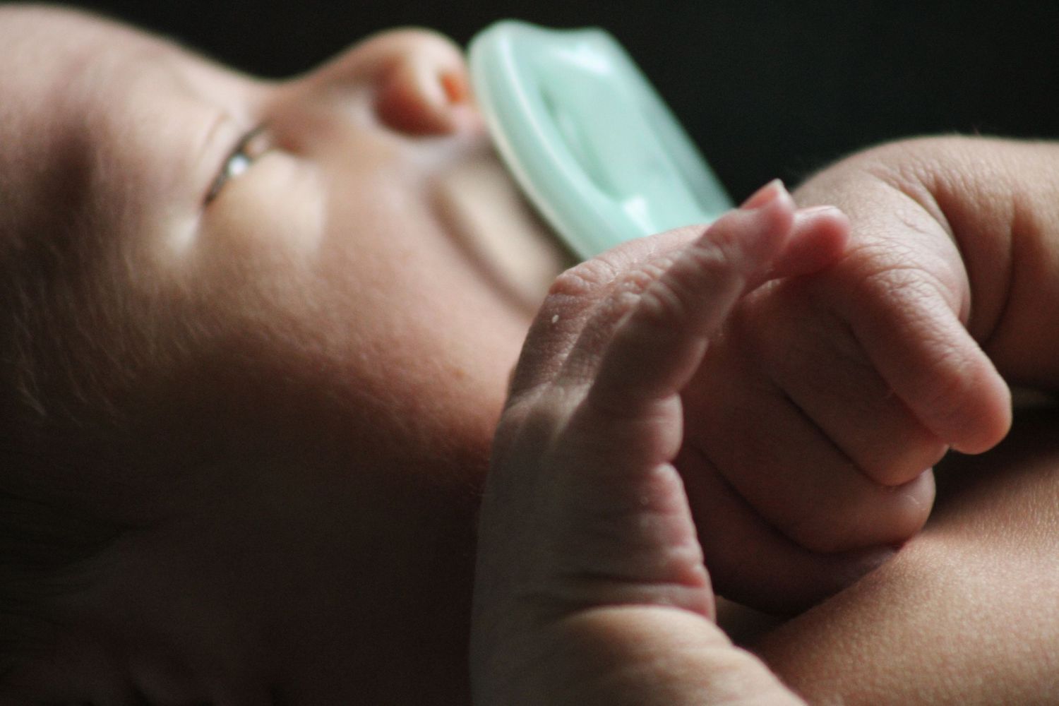 Close-up macro photography of a baby's tiny fingers and hand against a dark background.